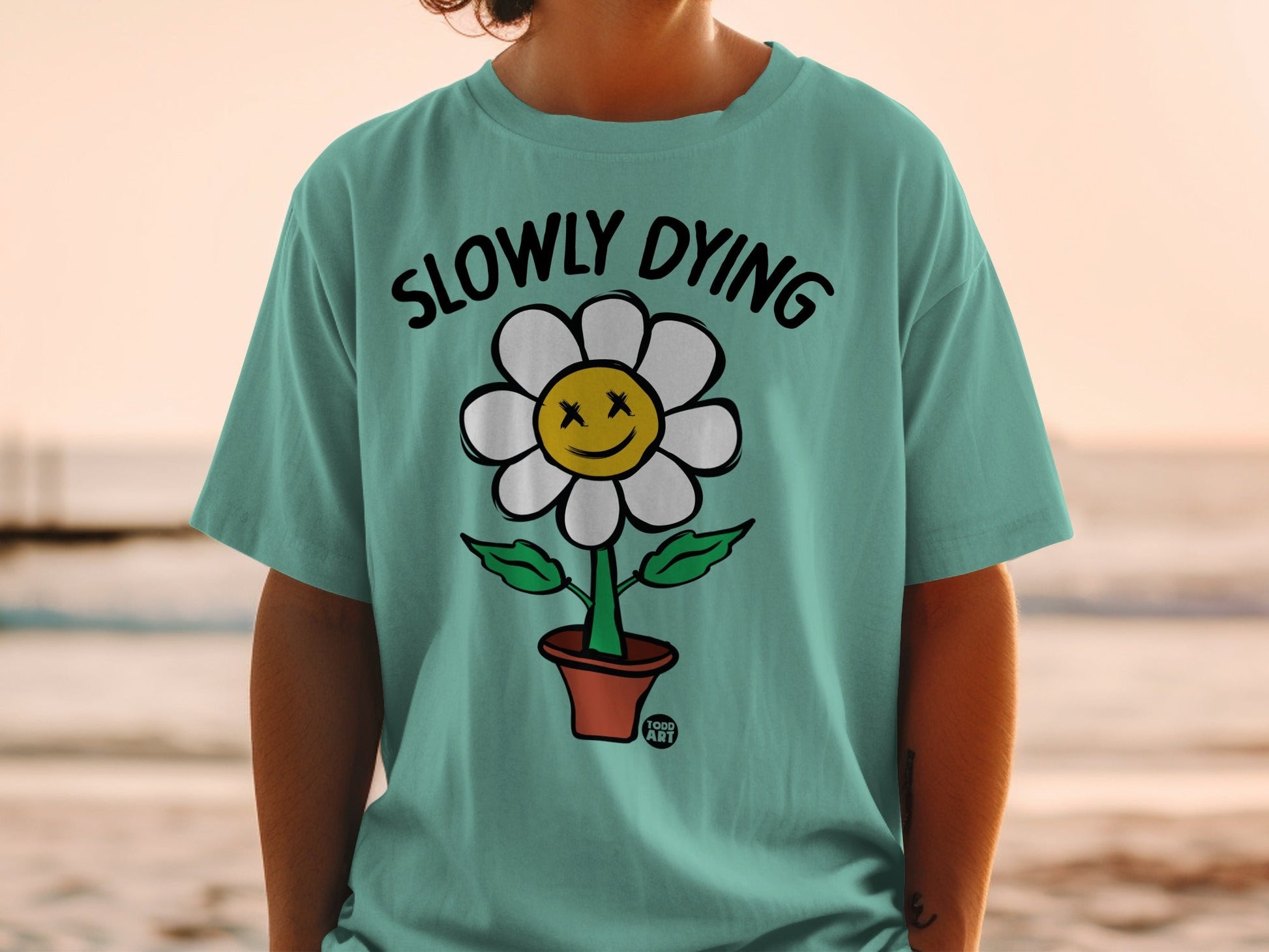 Teal t-shirt with cartoon flower graphic and text "SLOWLY DYING".