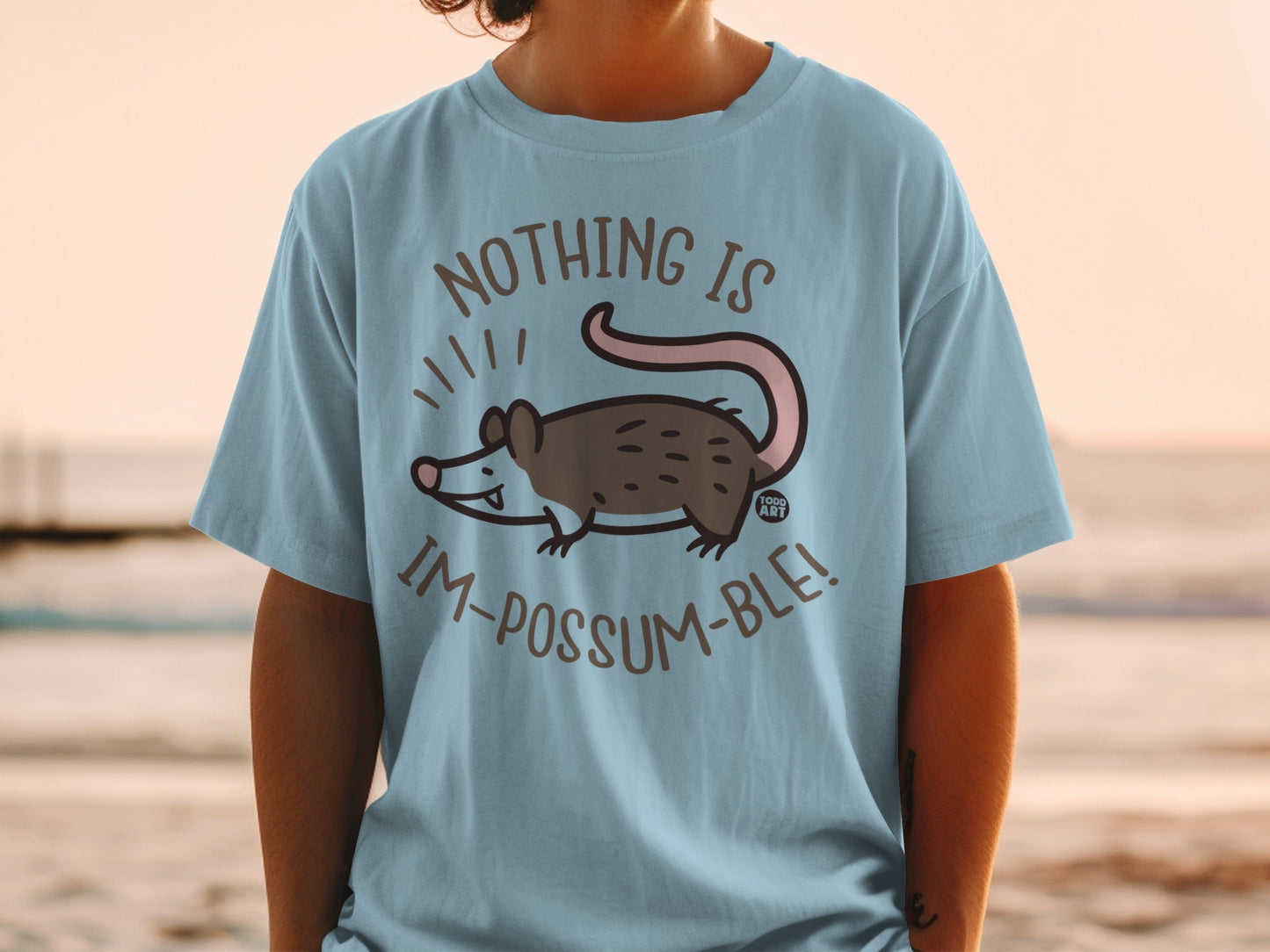 Light blue t-shirt with opossum illustration and "Nothing is Im-possum-ble!" text.