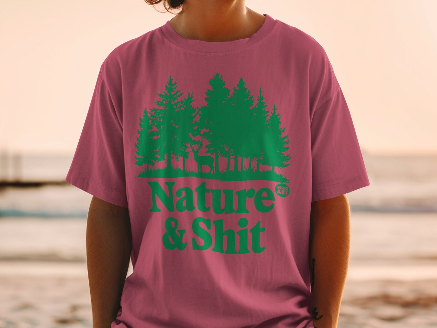 Pink t-shirt with green trees, deer, and "Nature & Shit" text.
