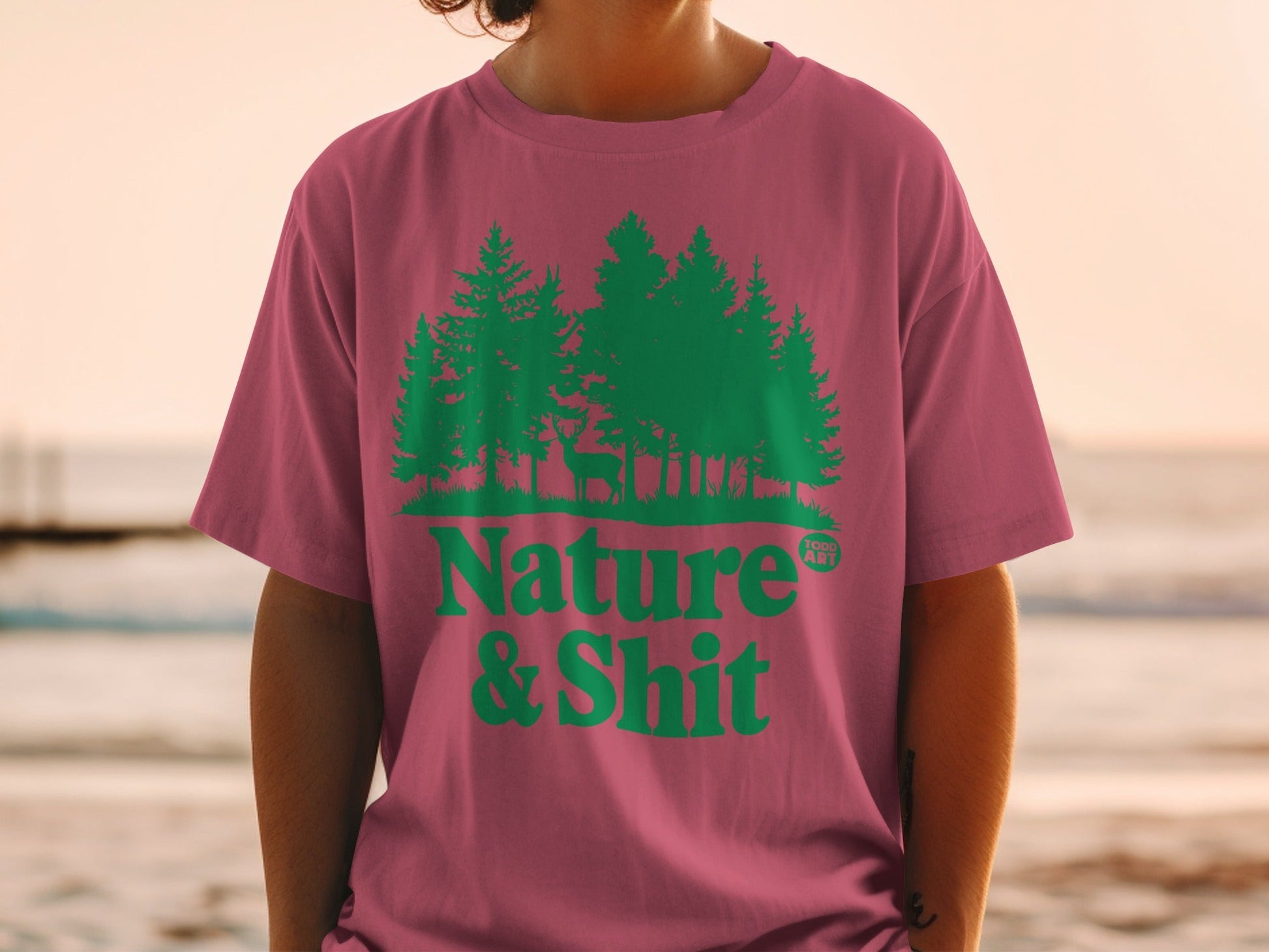 Pink t-shirt with green trees, deer, and "Nature & Shit" text.