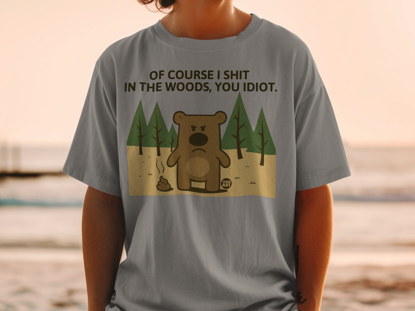 T-shirt with a cartoon bear shitting in the woods, text reads "Of course I shit in the woods, you idiot."