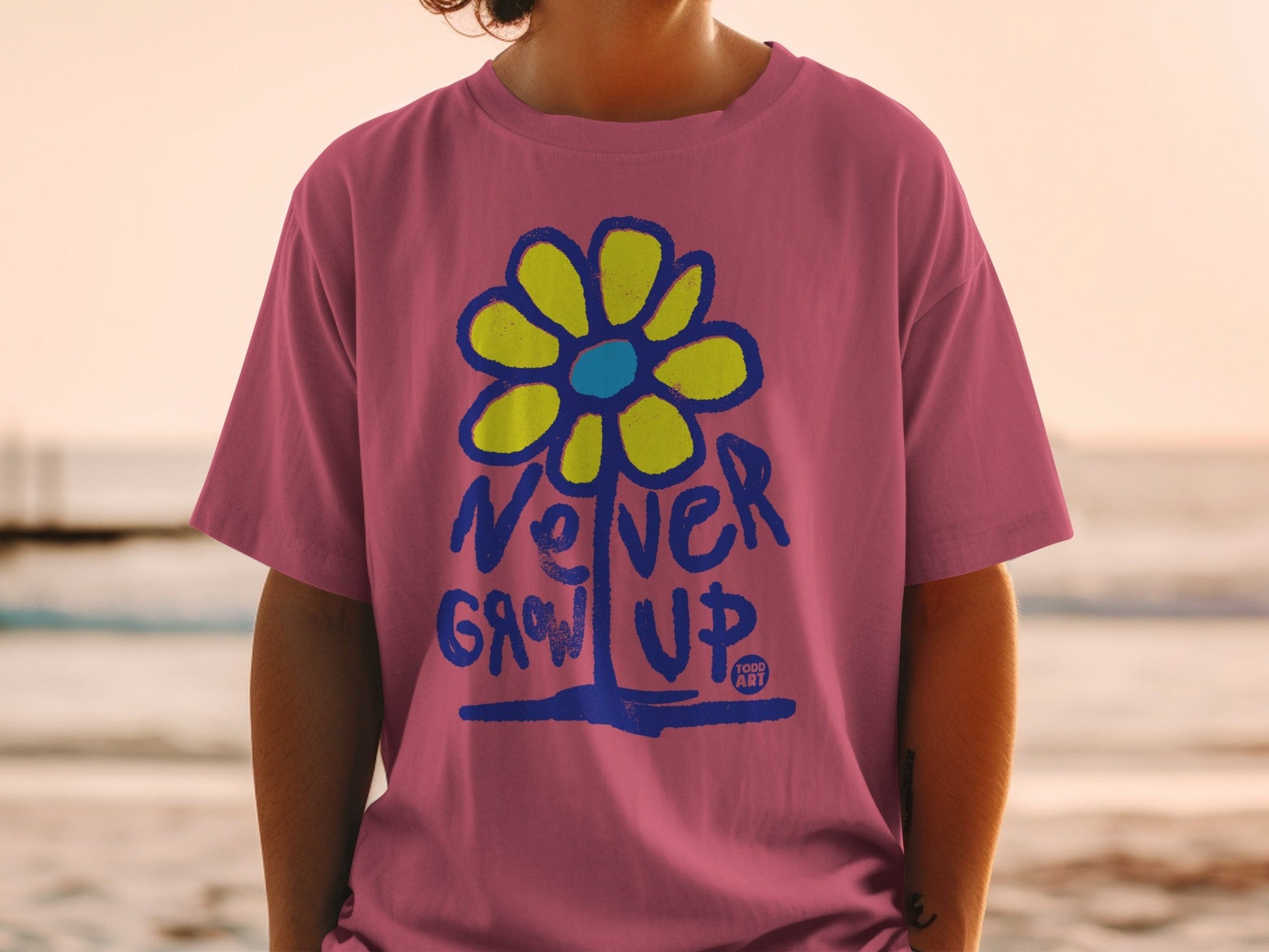 Pink t-shirt with yellow flower and blue text "NEVER GROW UP".