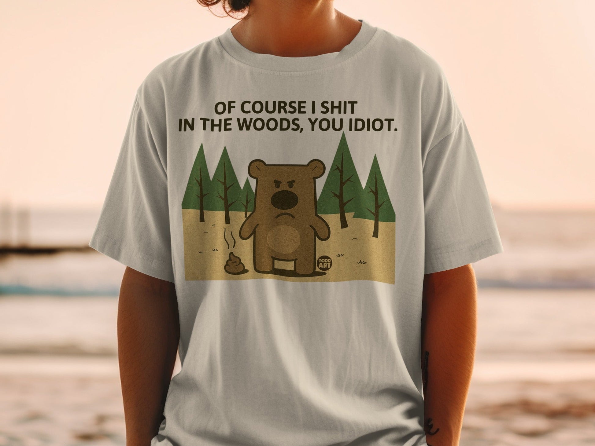 T-shirt with a cartoon bear defecating in the woods, text reads "Of course I shit in the woods, you idiot."