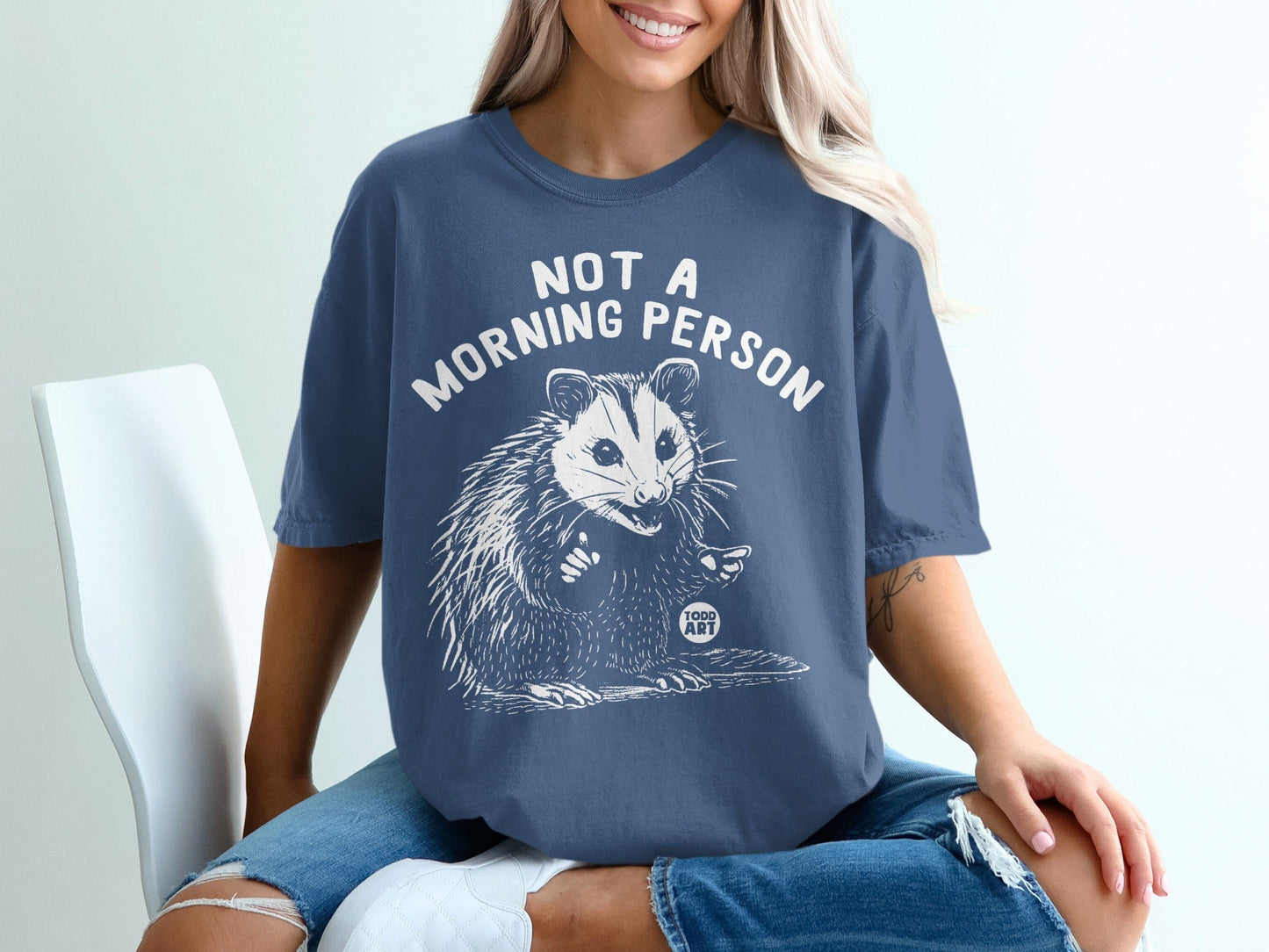 Woman wearing a blue t-shirt with a possum and "Not a Morning Person" text.