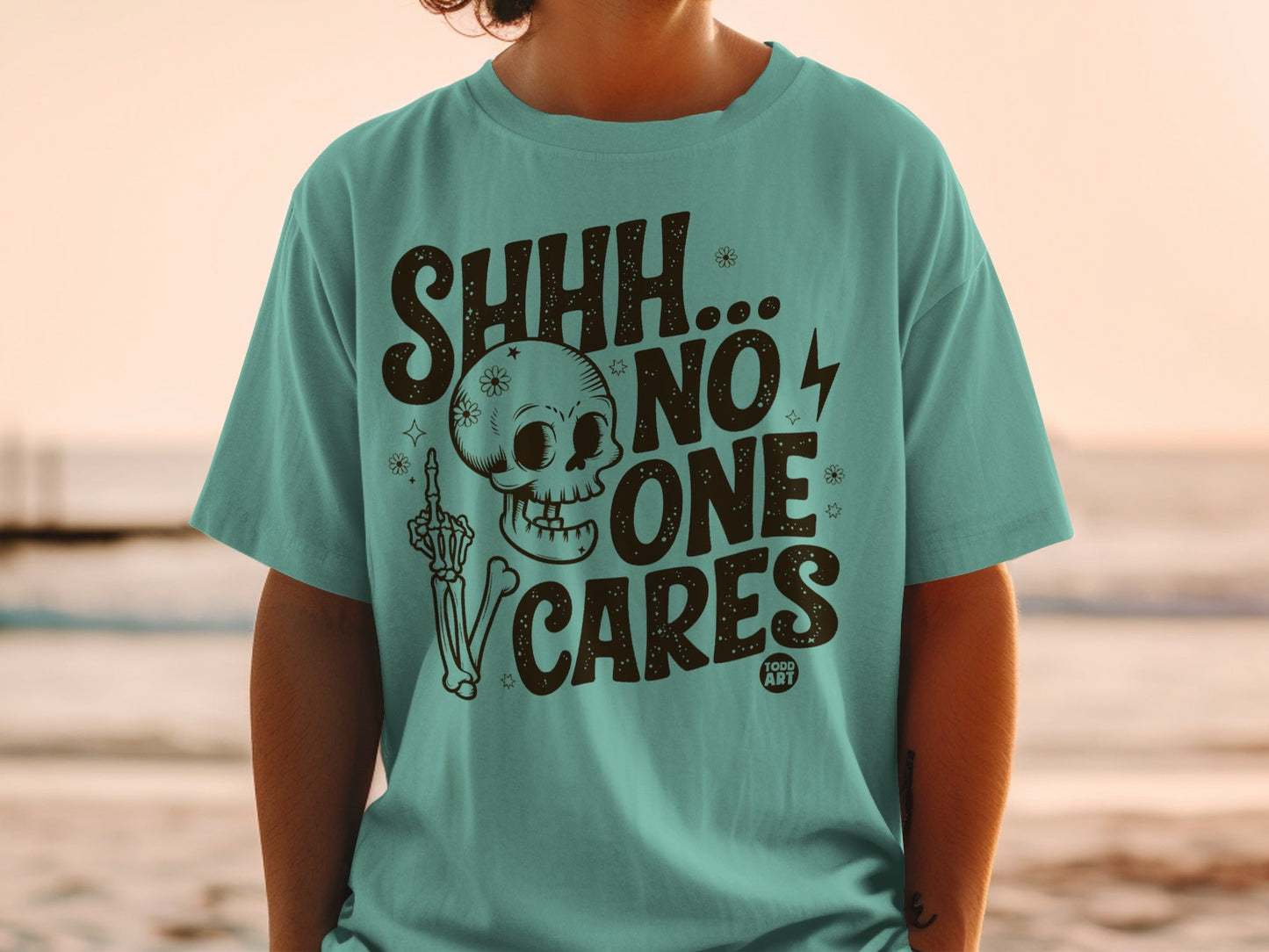 Teal t-shirt with skull, skeleton hand, and "SHHH... NO ONE CARES" text.