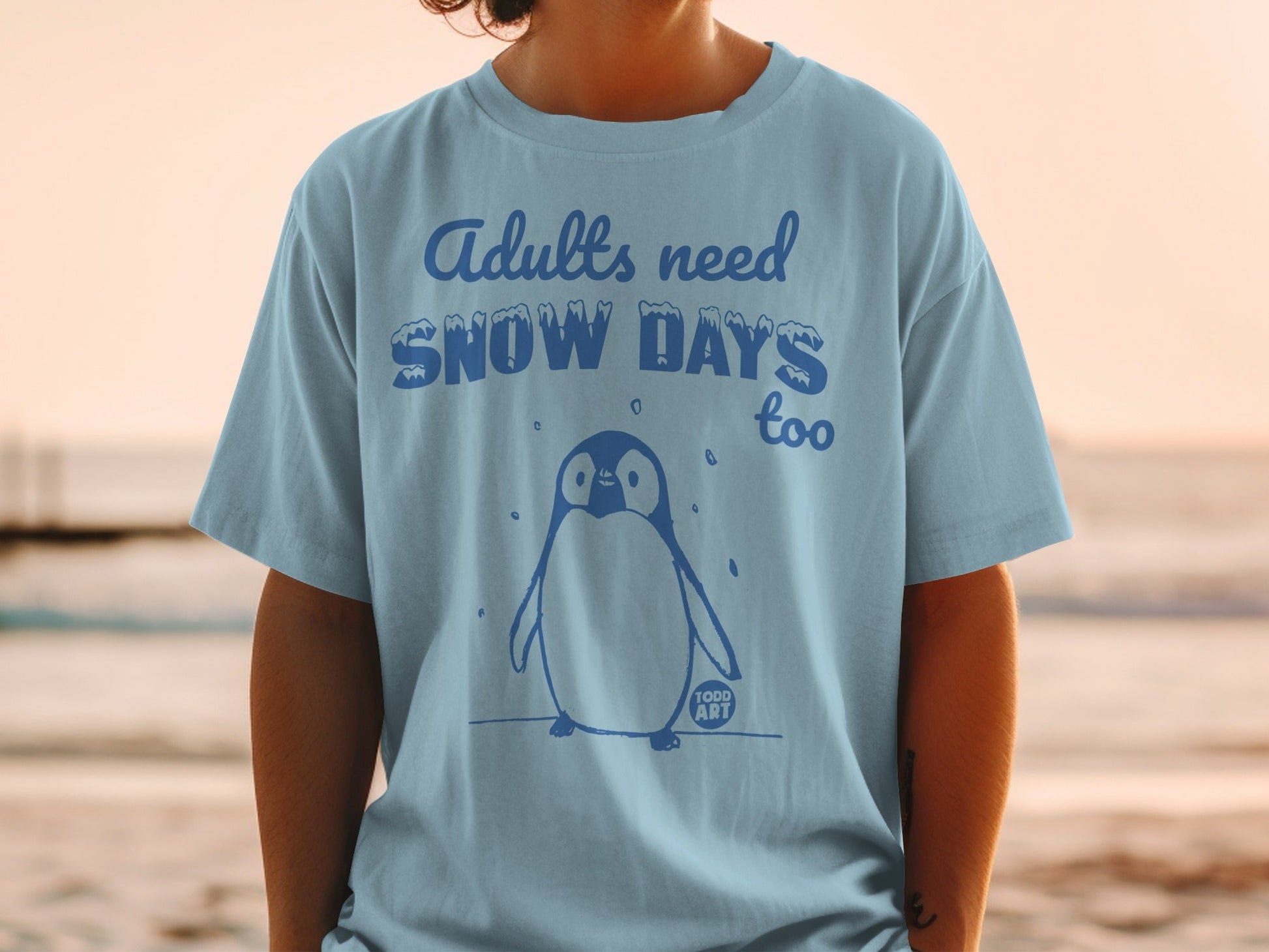 Blue t-shirt with a penguin and "Adults need snow days too" text.