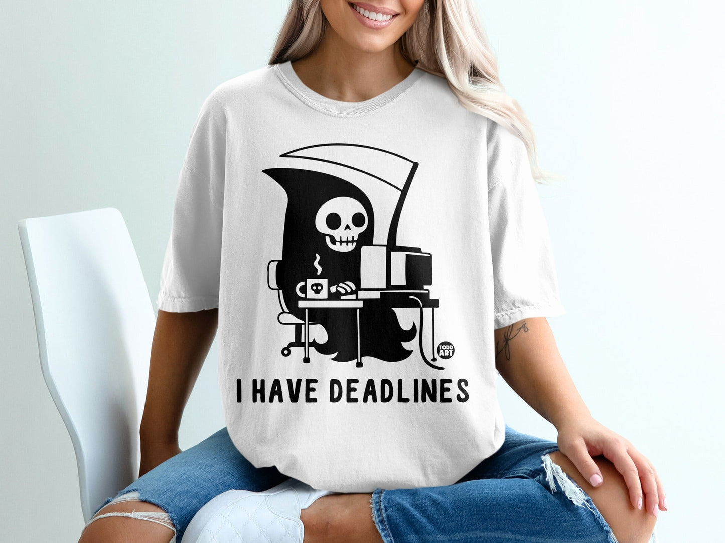 Grim reaper at a desk with coffee, text "I HAVE DEADLINES" on a t-shirt.
