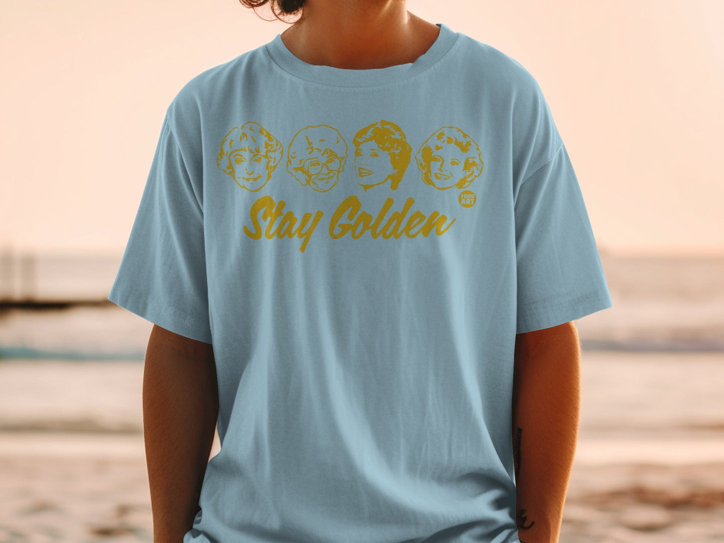 Light blue t-shirt with "Stay Golden" and four faces from The Golden Girls.