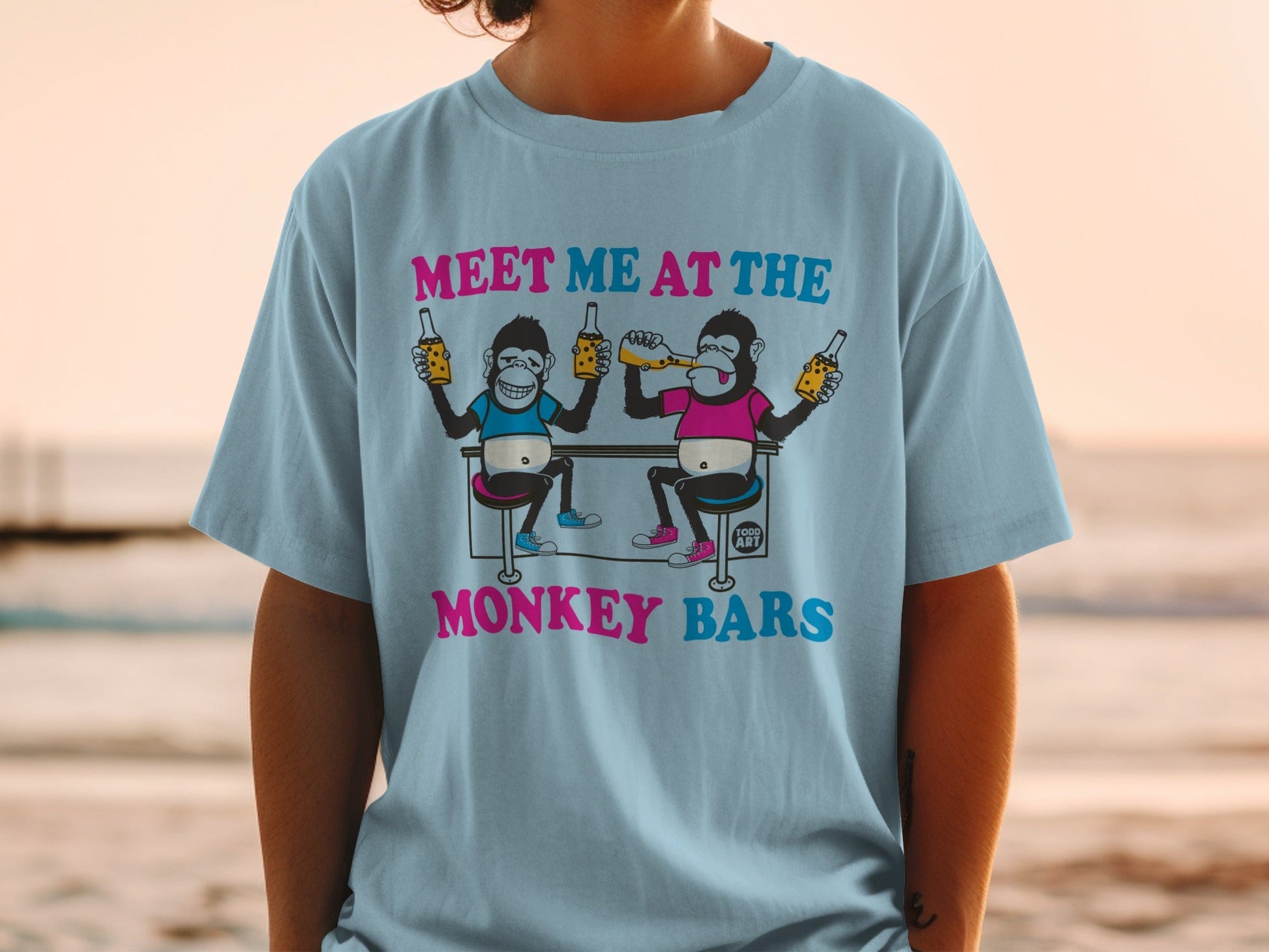 Light blue t-shirt with cartoon monkeys at a bar, text reads "MEET ME AT THE MONKEY BARS".