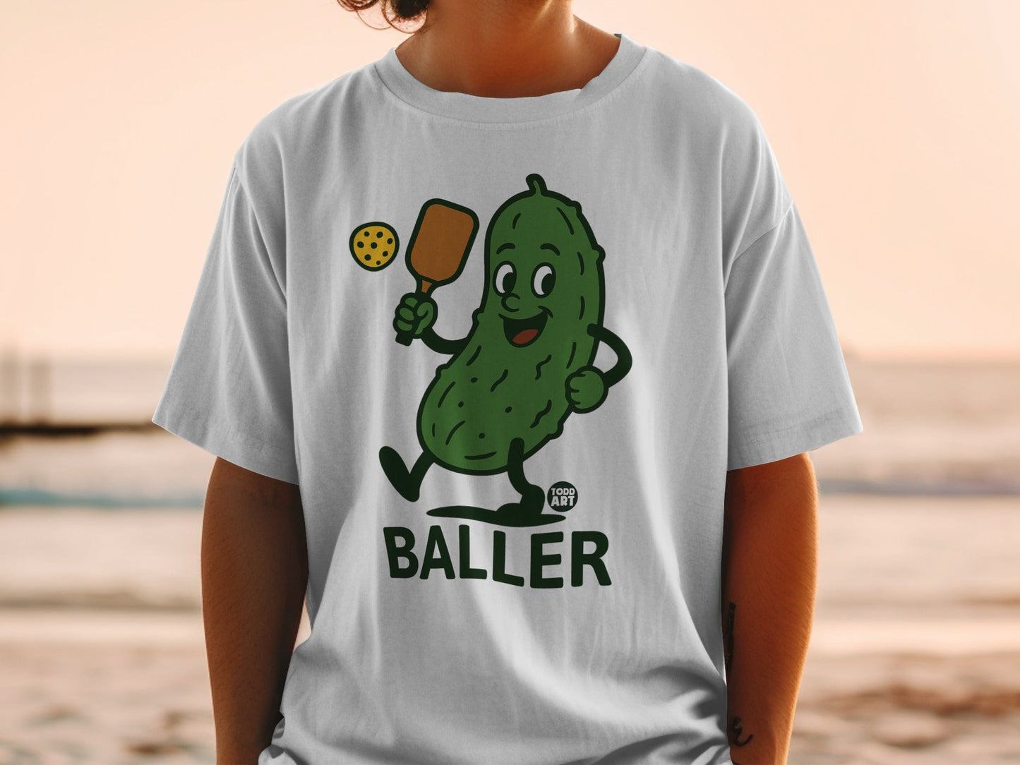 Cartoon pickle playing pickleball, wearing a "Food Art" logo.