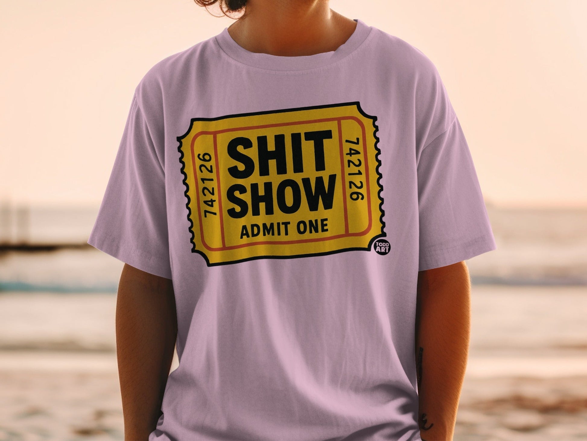 Lilac t-shirt with "SHIT SHOW ADMIT ONE" ticket design.