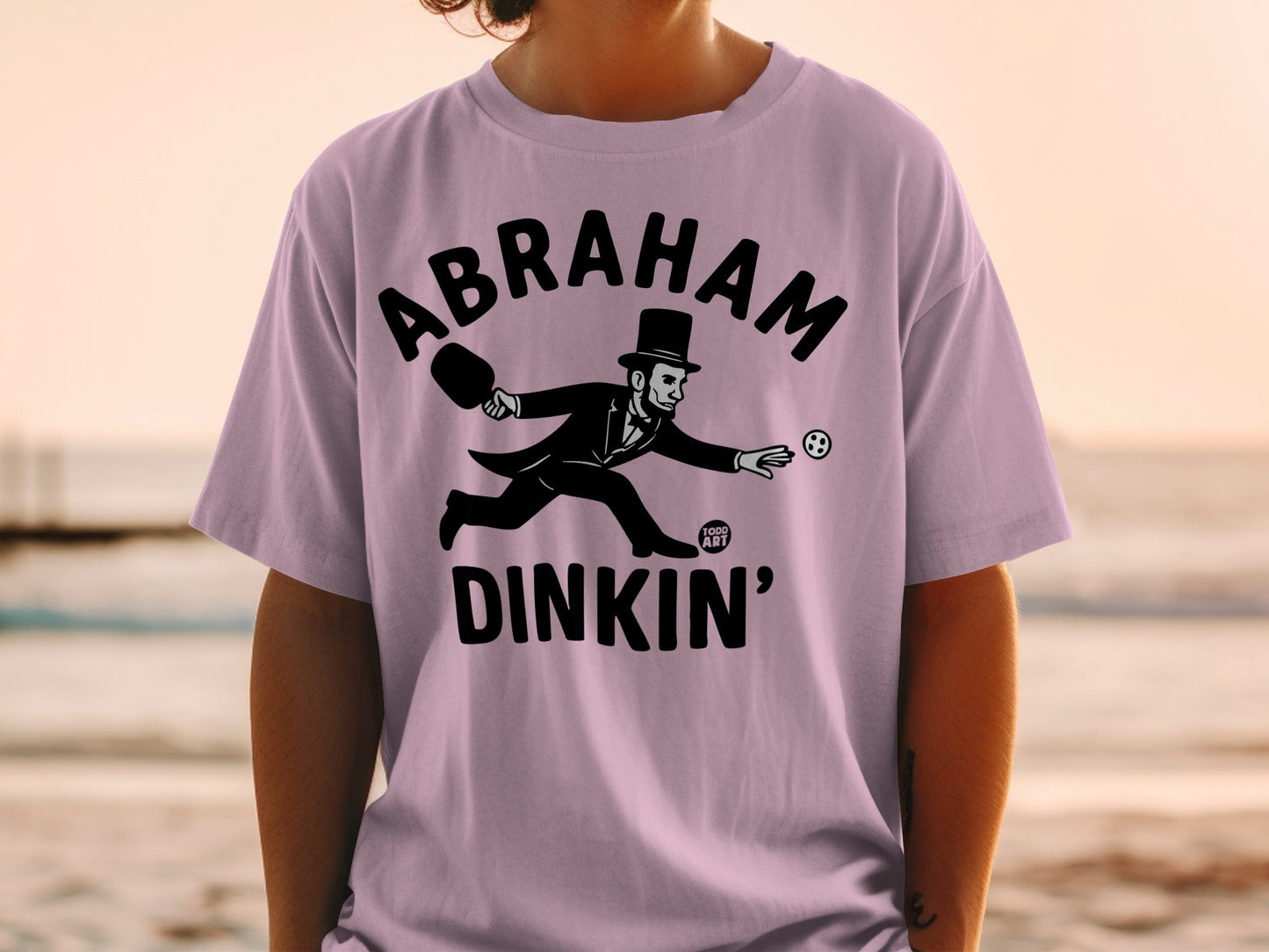 T-shirt with "Abraham Dinkin'" text and cartoon Abraham Lincoln playing paddleball.