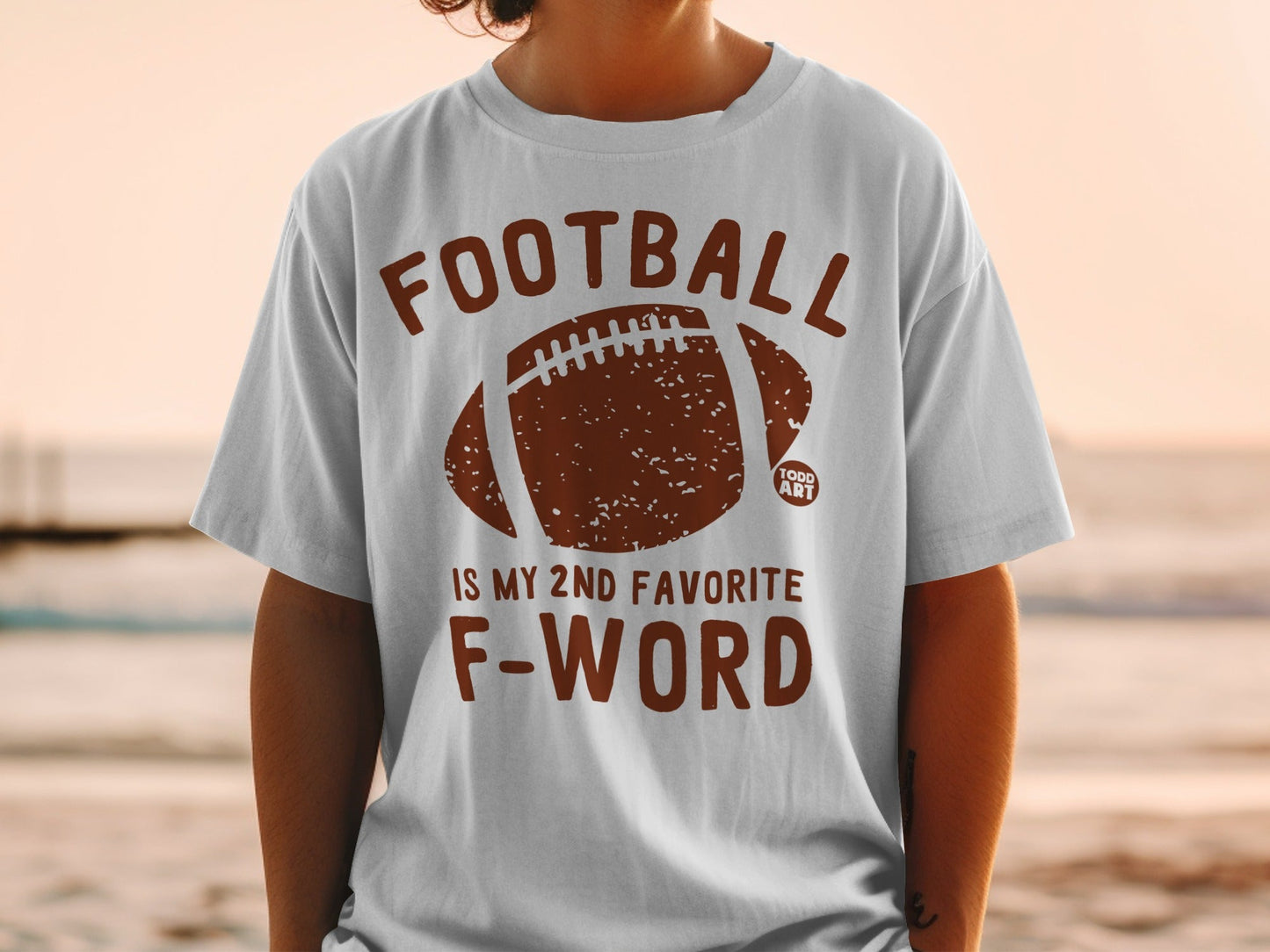 White t-shirt with brown distressed football graphic and text.