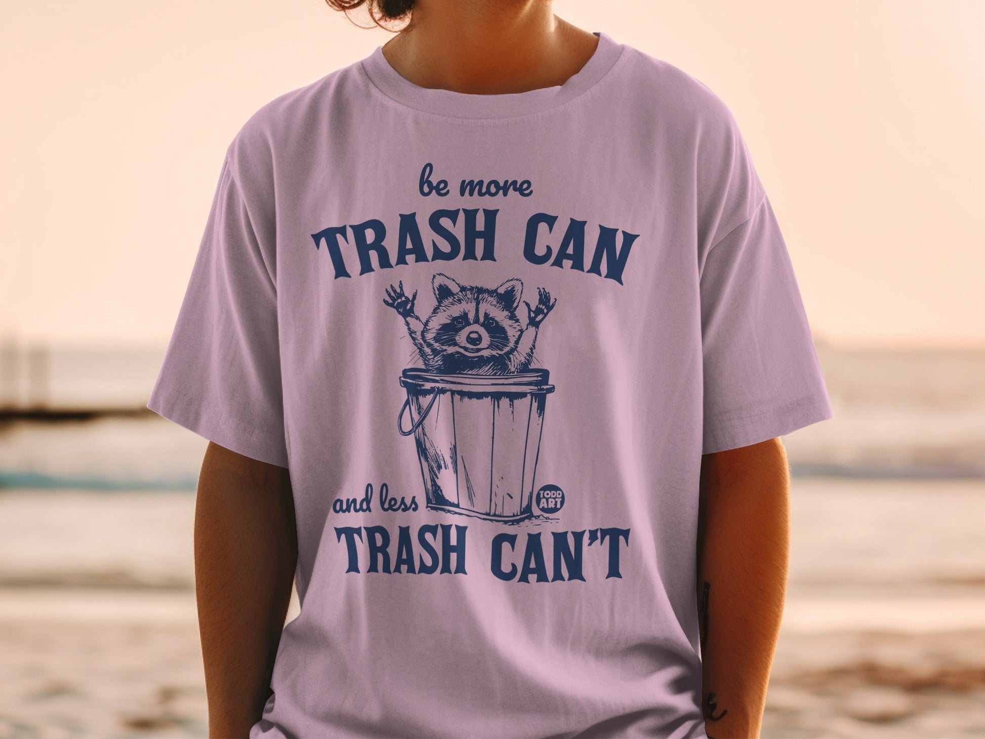 T-shirt with raccoon in trash can and text "be more TRASH CAN and less TRASH CAN'T".