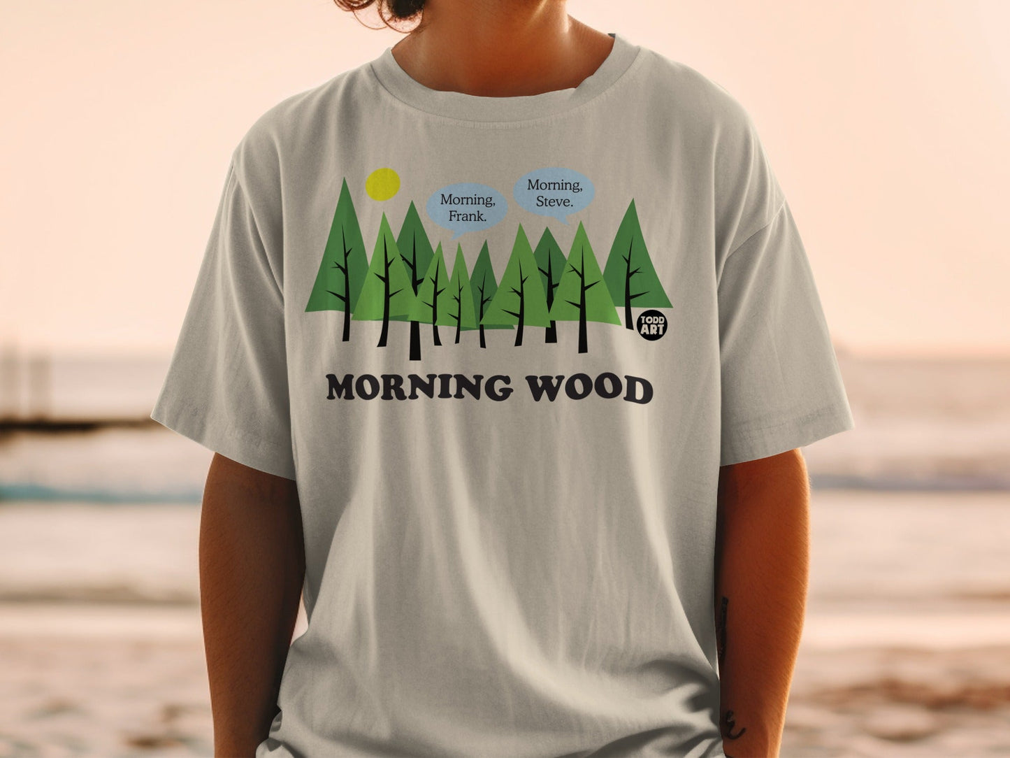 Light gray t-shirt with trees, "Morning, Frank. Morning, Steve." speech bubbles, and "MORNING WOOD" text.