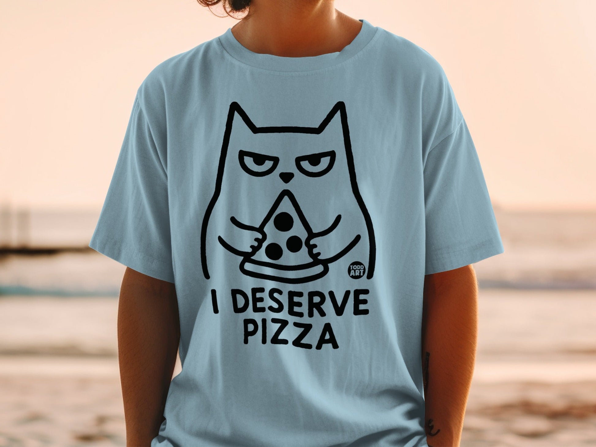 Light blue t-shirt with black outline of a grumpy cat eating pizza, text reads "I DESERVE PIZZA".