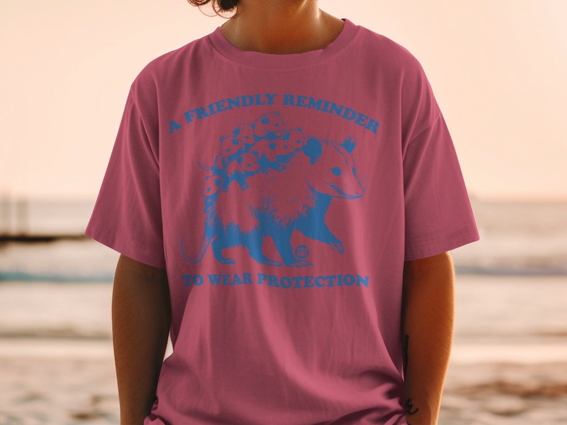 T-shirt with blue graphic of an opossum and the text "A FRIENDLY REMINDER TO WEAR PROTECTION".