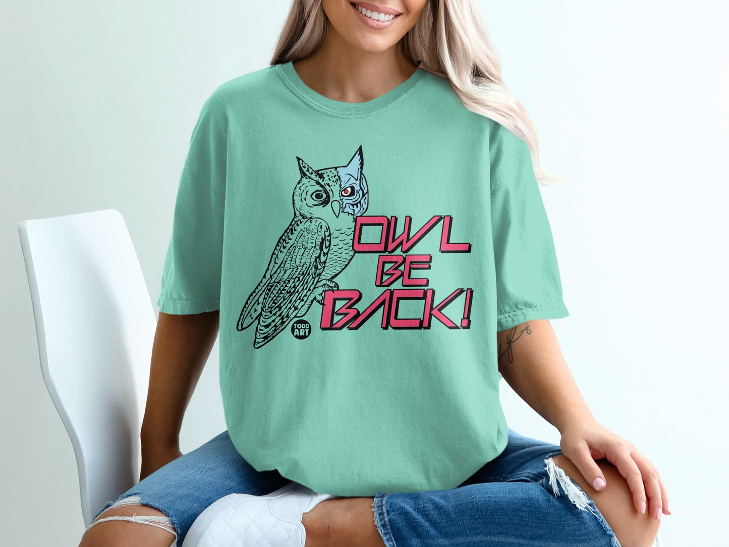 Teal t-shirt with "OWL BE BACK!" text and owl graphic on white chair.