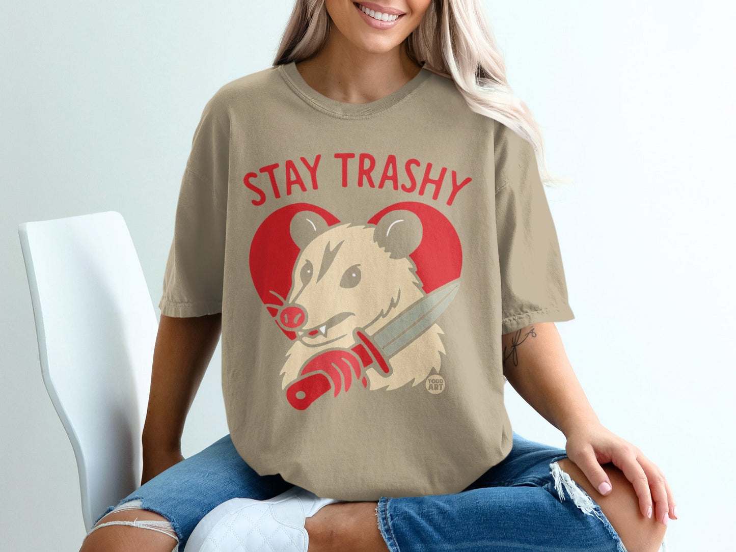 Stay Trashy graphic tee with a possum holding a knife in front of a heart.