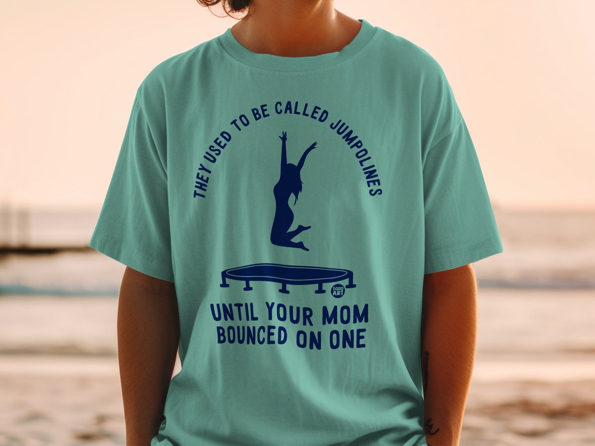 Teal t-shirt with jumping silhouette and text: "They used to be called jumpolines until your mom bounced on one."