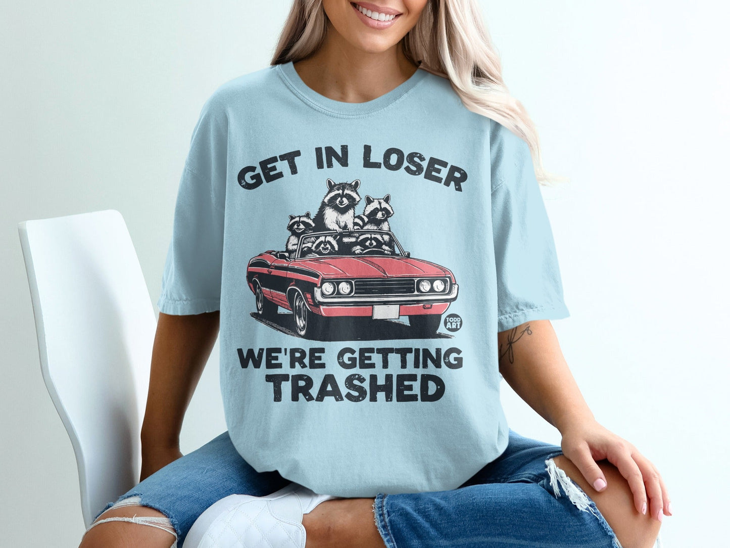 Light blue t-shirt with "GET IN LOSER WE'RE GETTING TRASHED" and raccoons in a car.