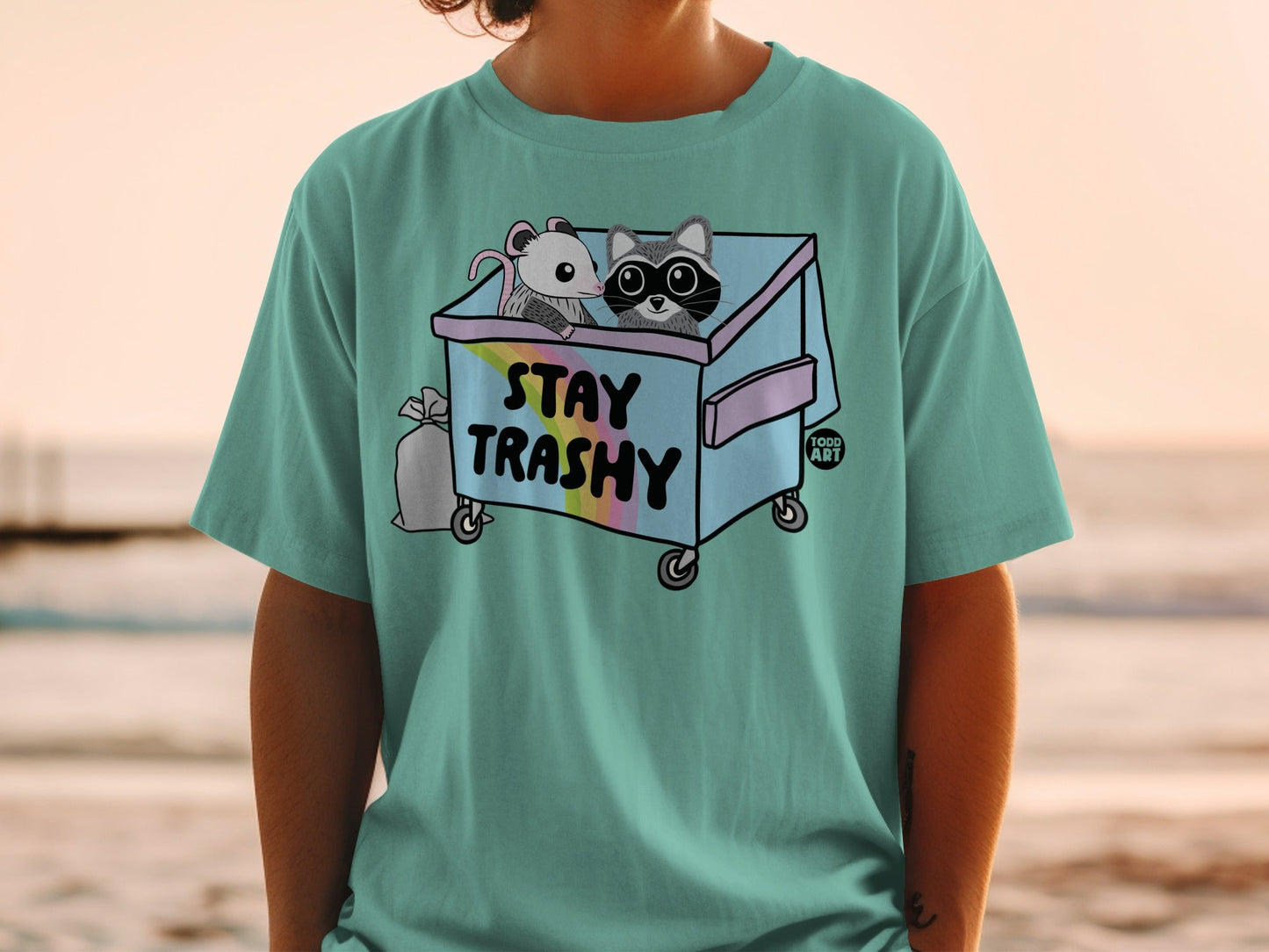 Trash panda and opossum in trash can graphic on teal t-shirt.