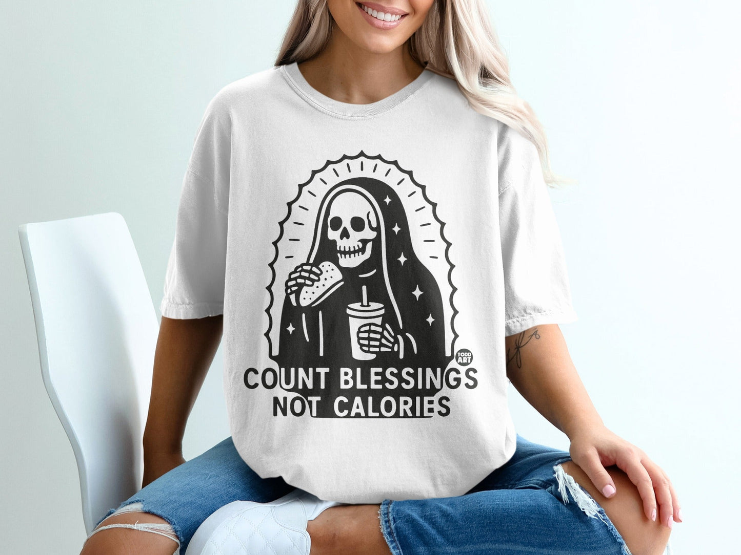 White t-shirt with skeleton graphic holding burger and drink, "COUNT BLESSINGS NOT CALORIES" text.