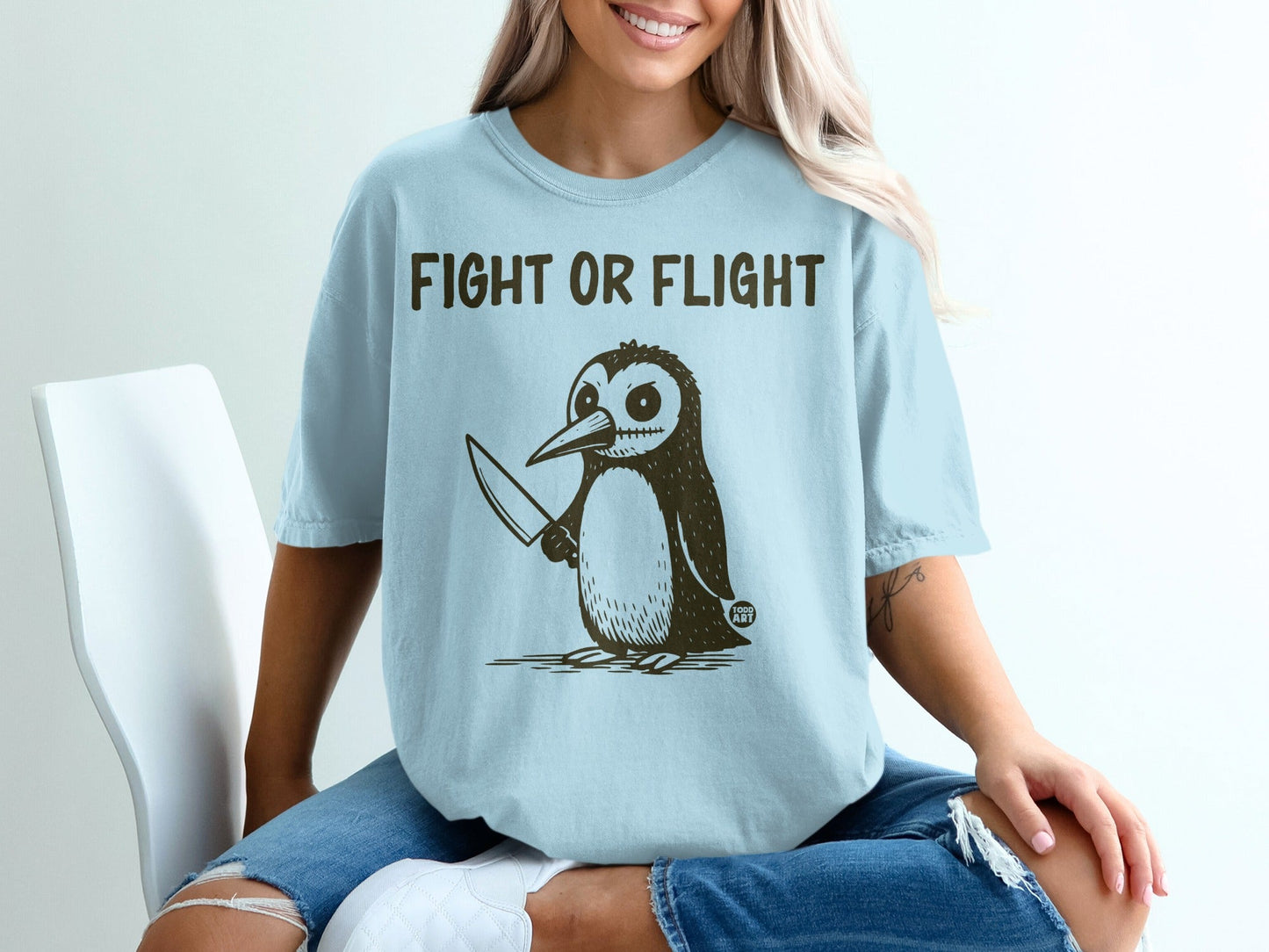 Light blue t-shirt with a cartoon penguin holding a knife and text "FIGHT OR FLIGHT".