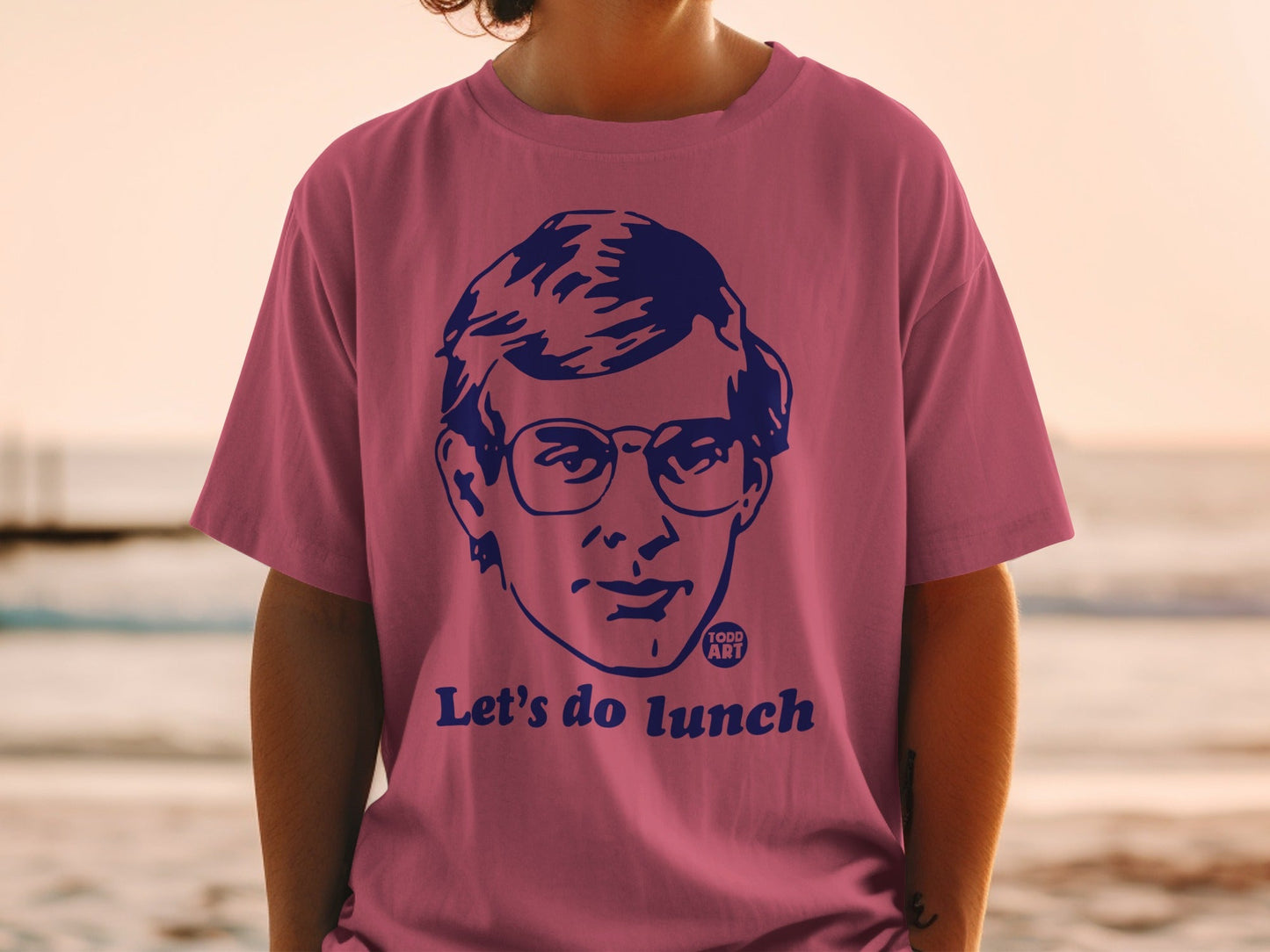 Pink t-shirt with a navy blue graphic of a person's face and the text "Let's do lunch".