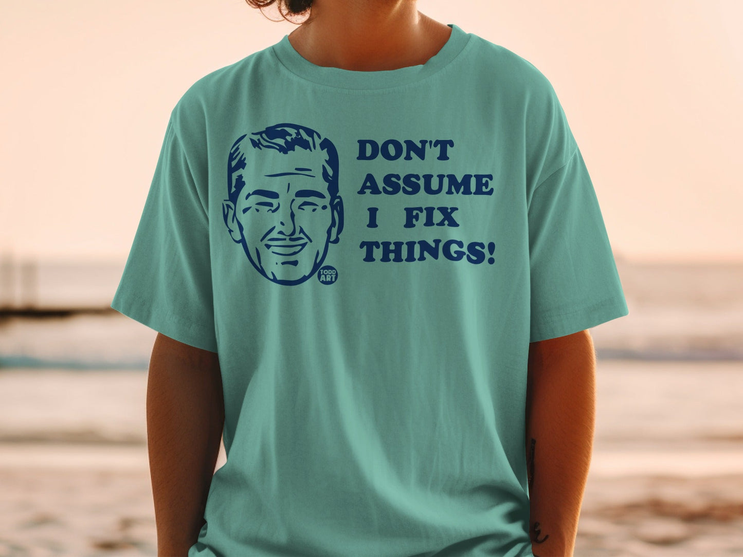 Teal t-shirt with cartoon man's face and text "DON'T ASSUME I FIX THINGS!".