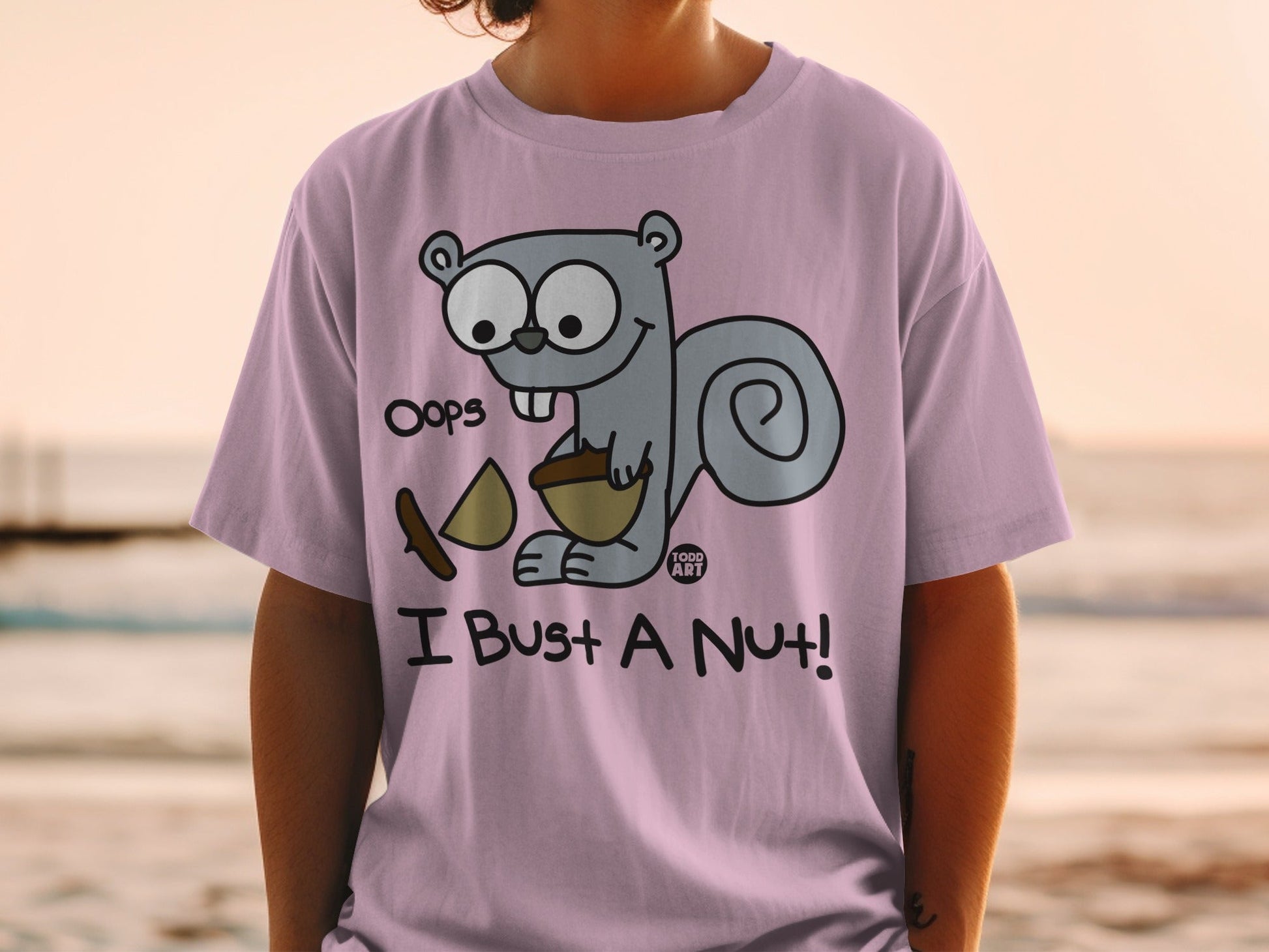 Pink t-shirt with cartoon squirrel holding a nut, text reads "Oops I Bust a Nut!".