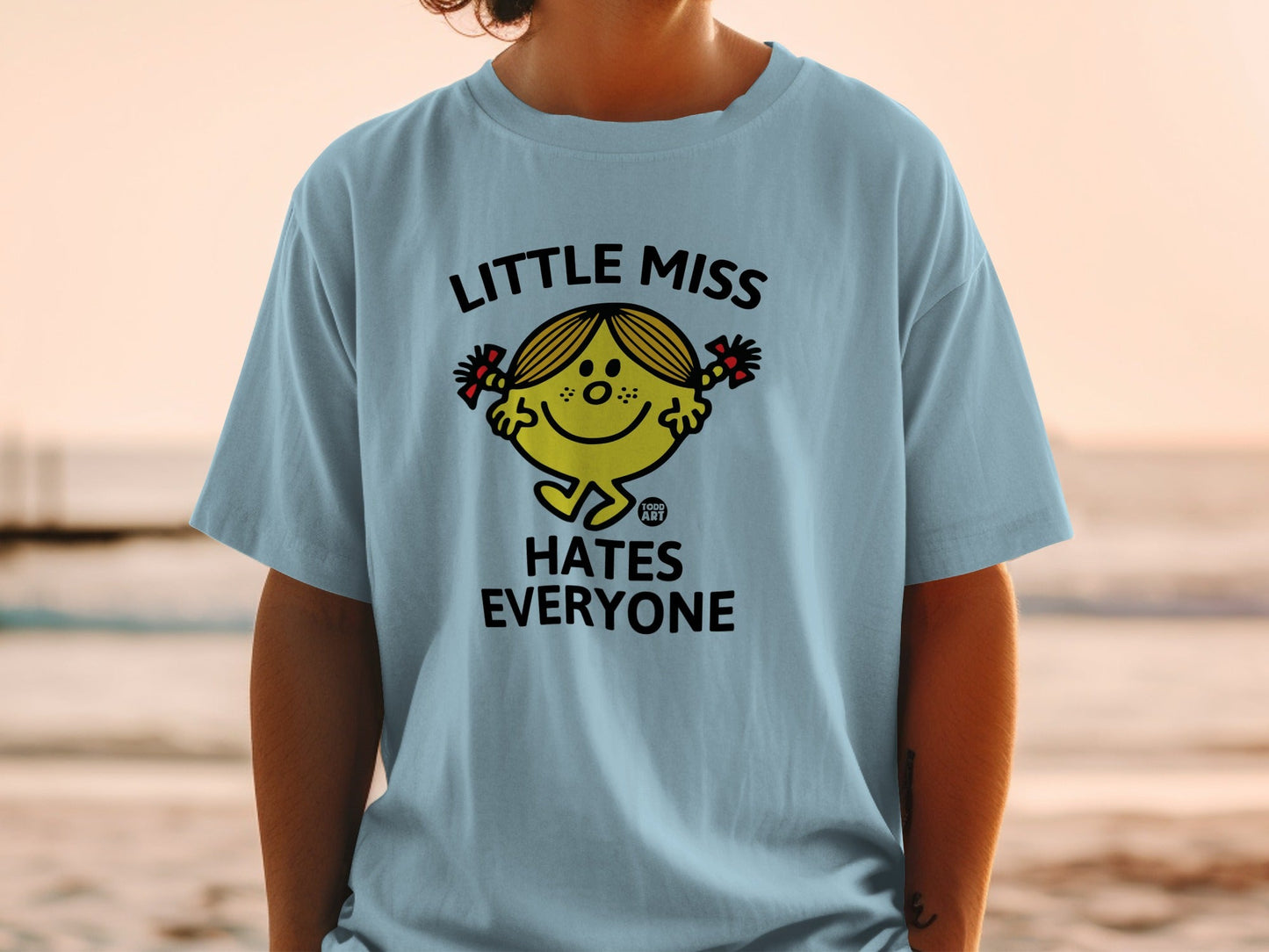 Light blue t-shirt with "Little Miss Hates Everyone" cartoon graphic.