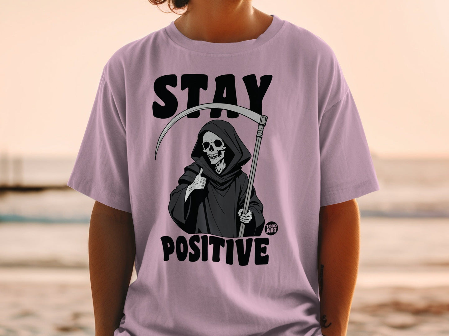 Grim reaper giving a thumbs up on a pink t-shirt, "STAY POSITIVE".