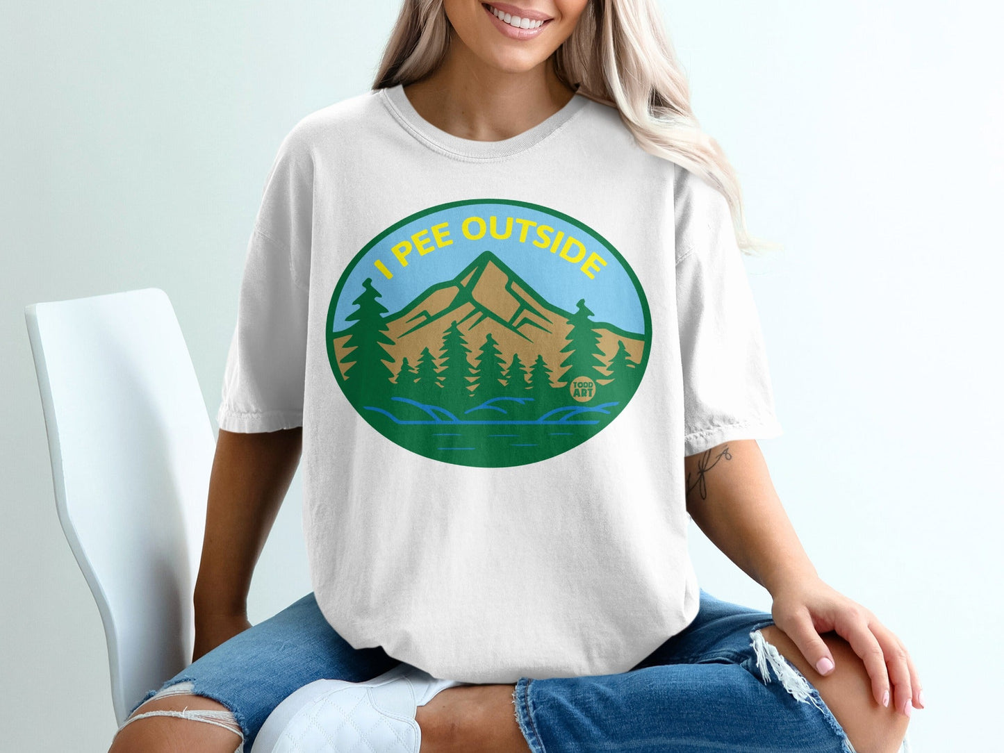 White t-shirt with "I pee outside" text and a mountain landscape graphic.