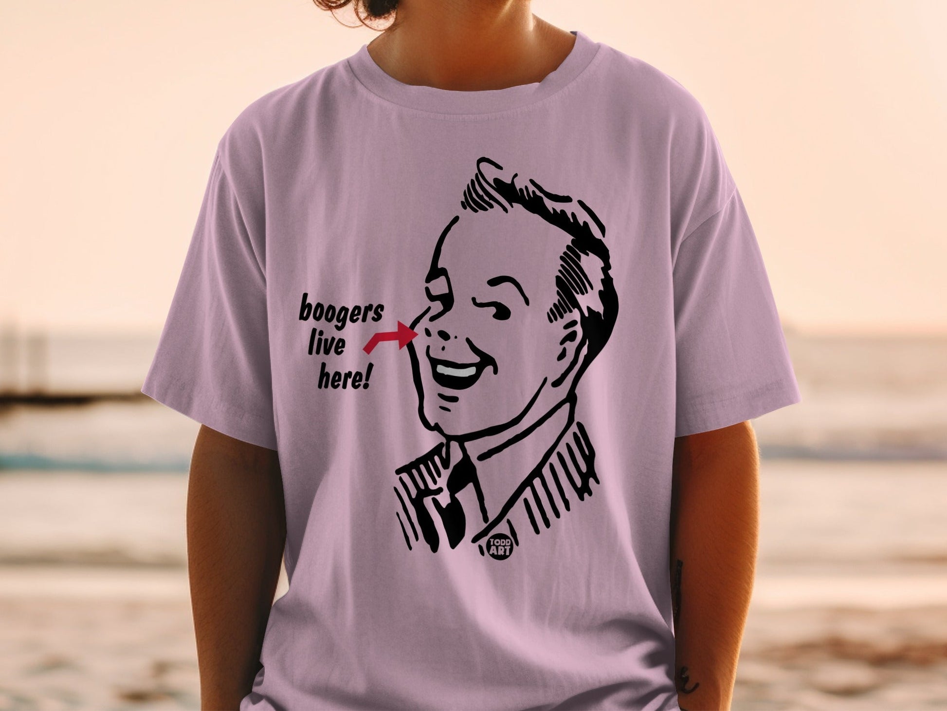 Pink t-shirt with cartoon man pointing to text "boogers live here".