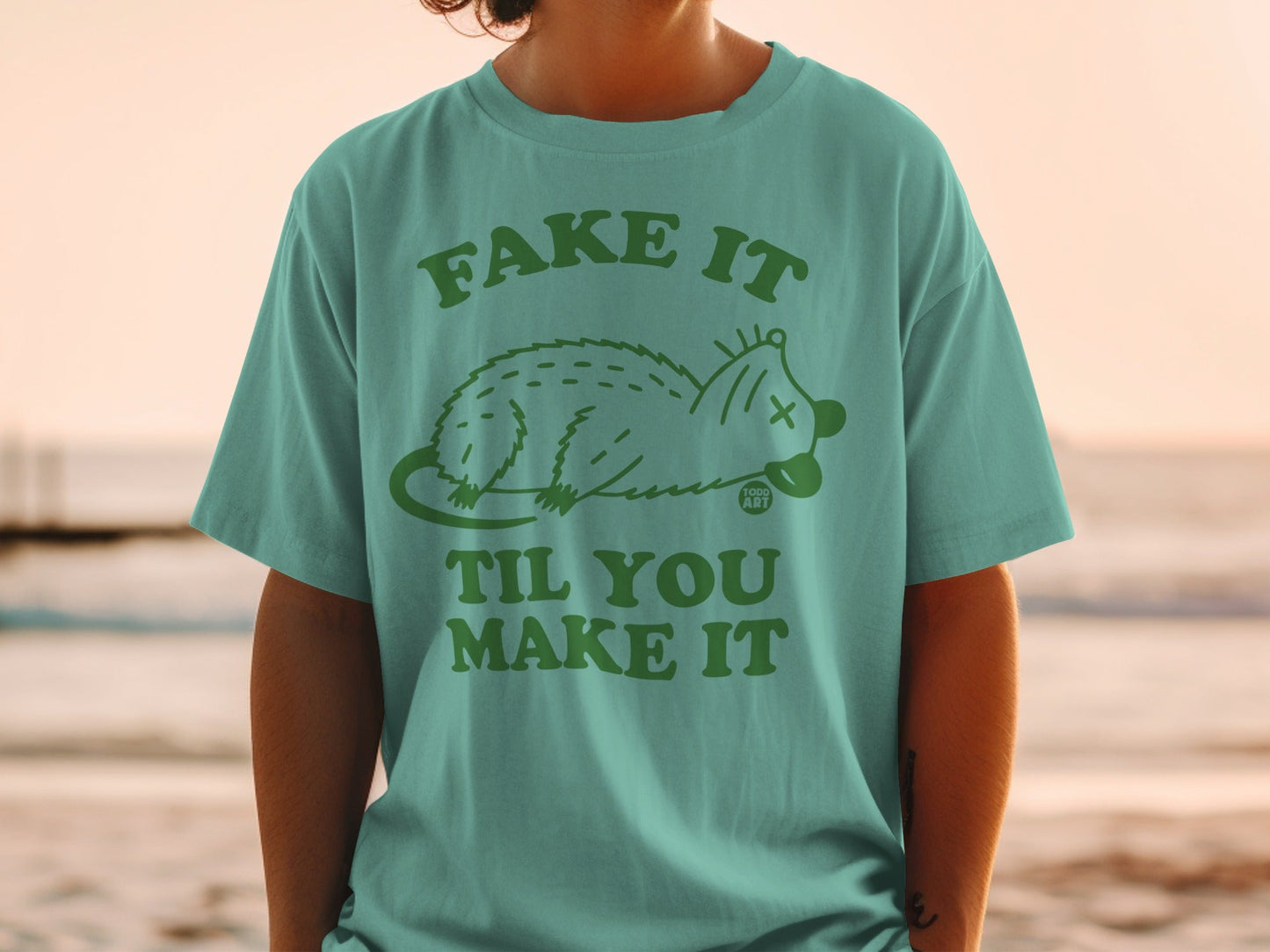 Teal t-shirt with green possum graphic and "Fake It Til You Make It" text.
