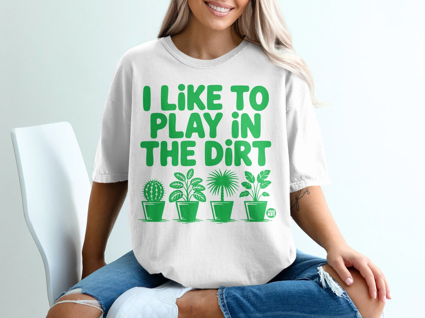 White t-shirt with green text "I LIKE TO PLAY IN THE DIRT" and potted plants.