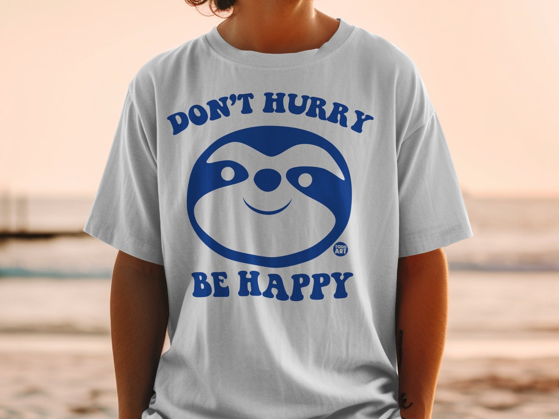 White t-shirt with blue sloth graphic, "DON'T HURRY BE HAPPY" text.