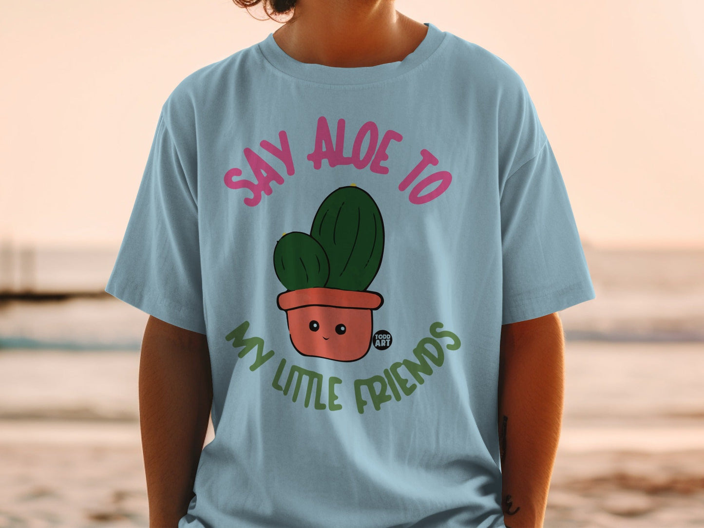 Light blue t-shirt with cartoon cactus saying "Say Aloe to My Little Friends."