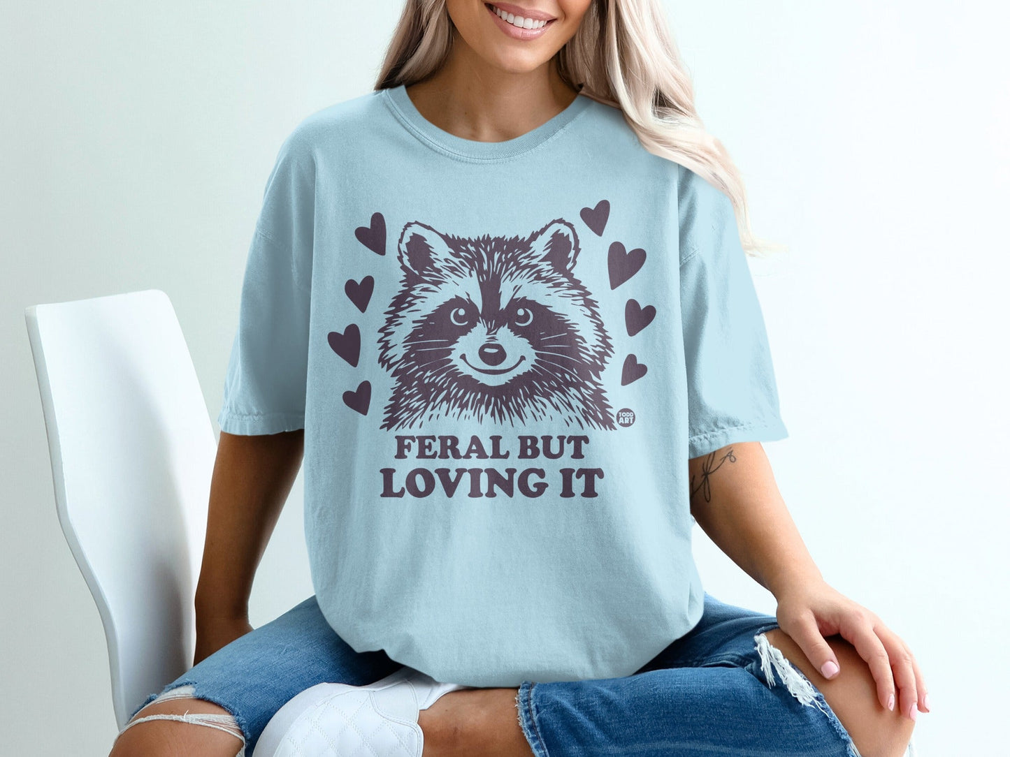 Light blue t-shirt with a raccoon graphic and "Feral But Loving It" text.