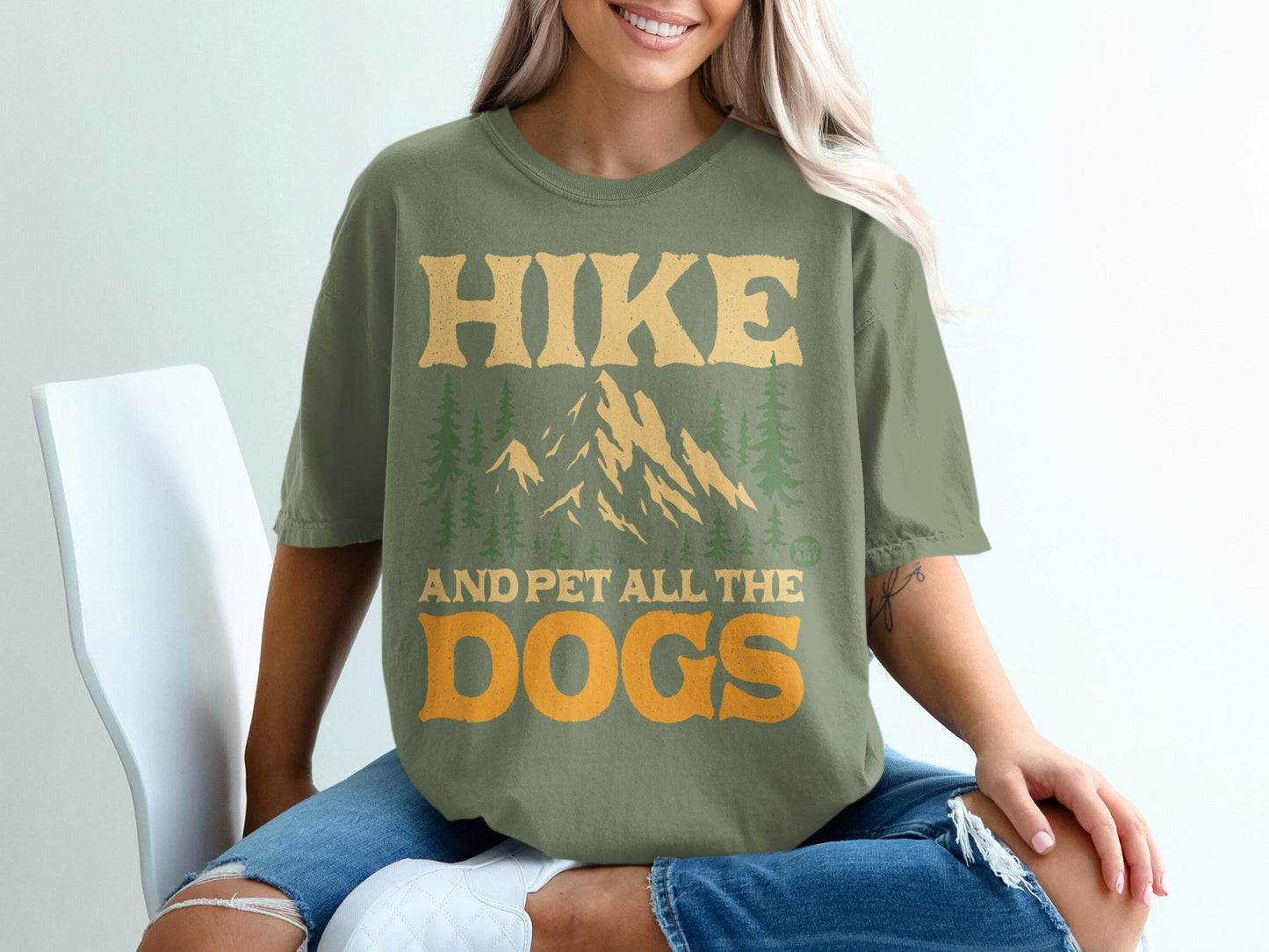 Green t-shirt with mountains and trees, reading "Hike and pet all the dogs."