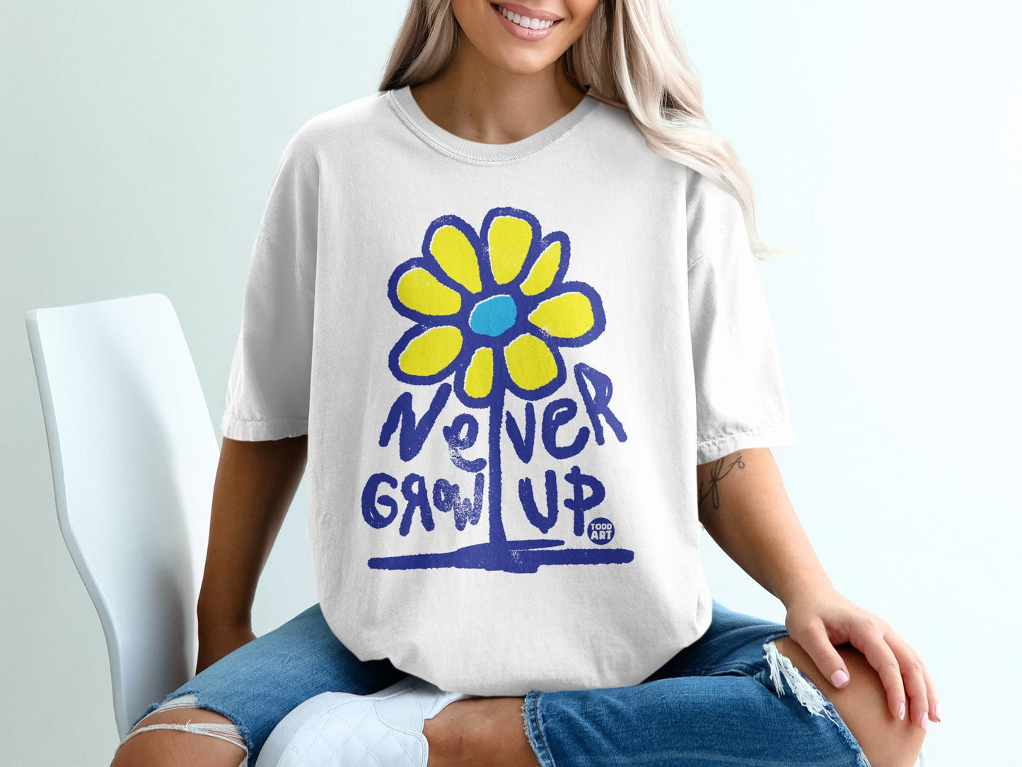 White t-shirt with blue "Never Grow Up" text and yellow flower graphic.