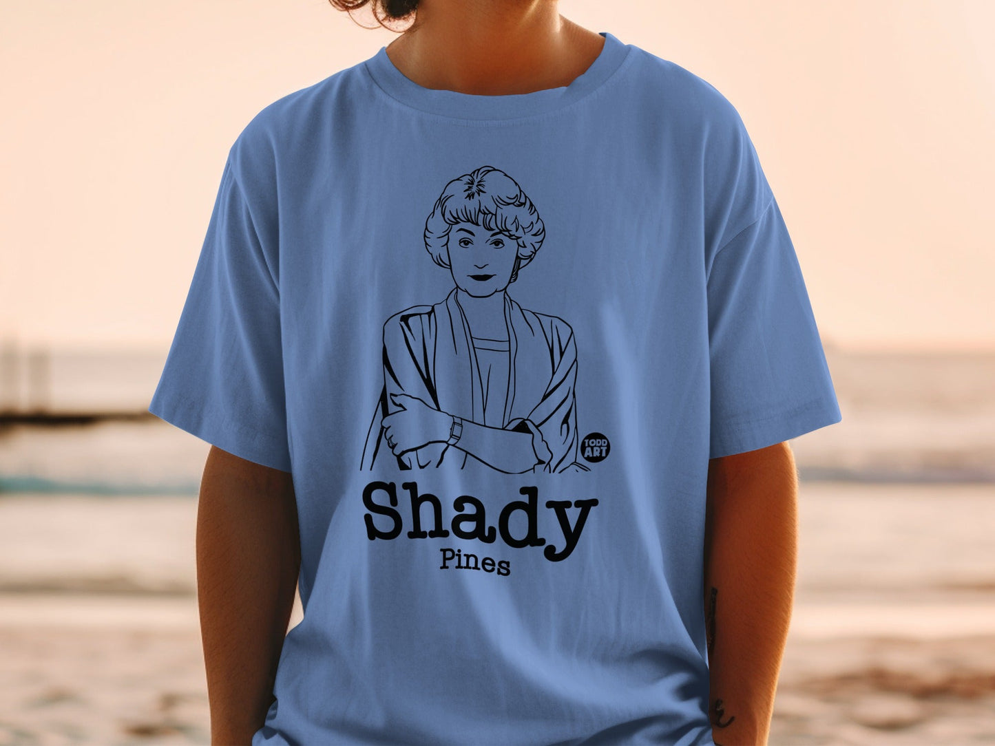 Blue t-shirt with line art portrait of woman, "Shady Pines" text.