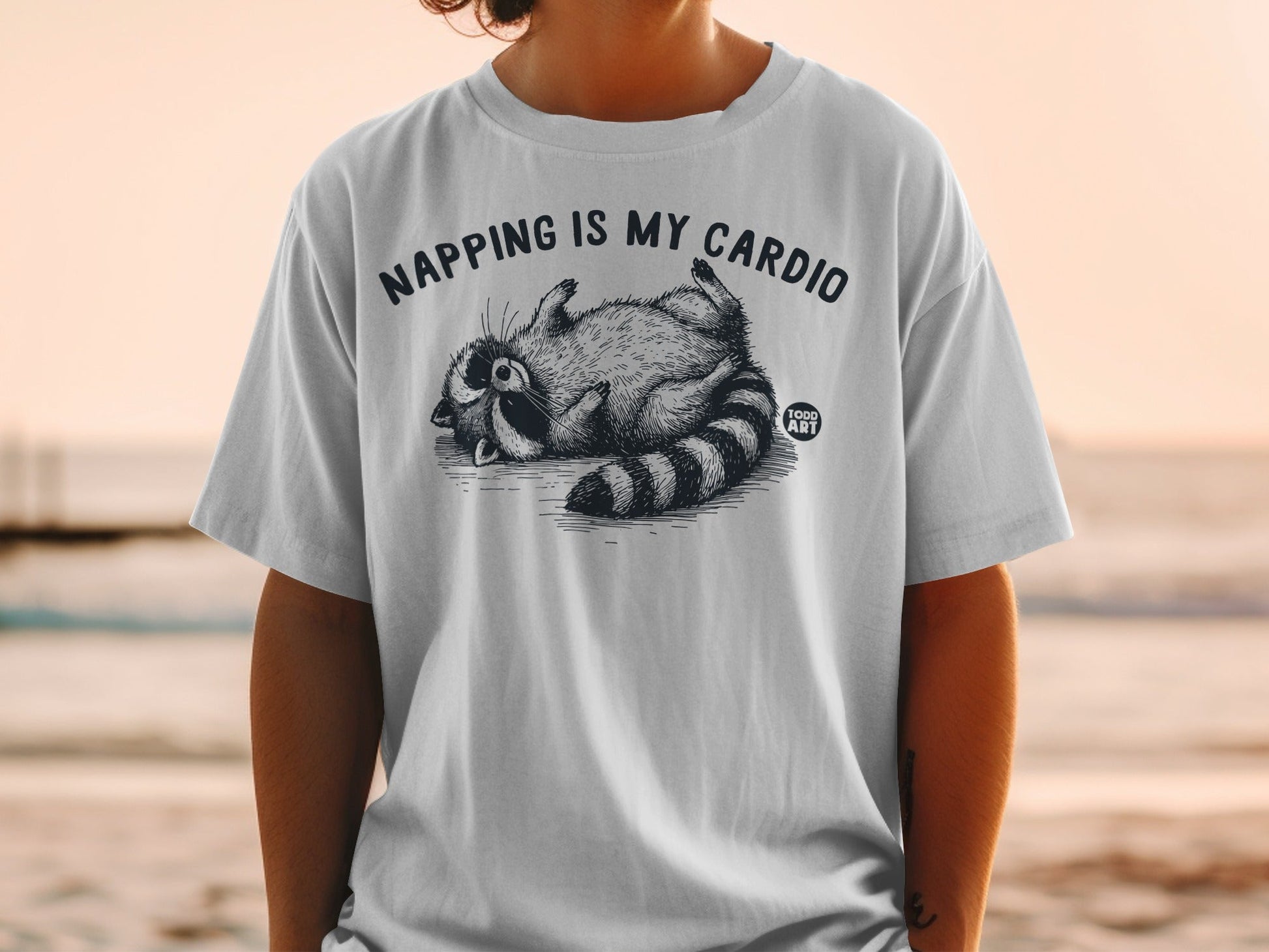 White t-shirt with raccoon graphic and "NAPPING IS MY CARDIO" text.