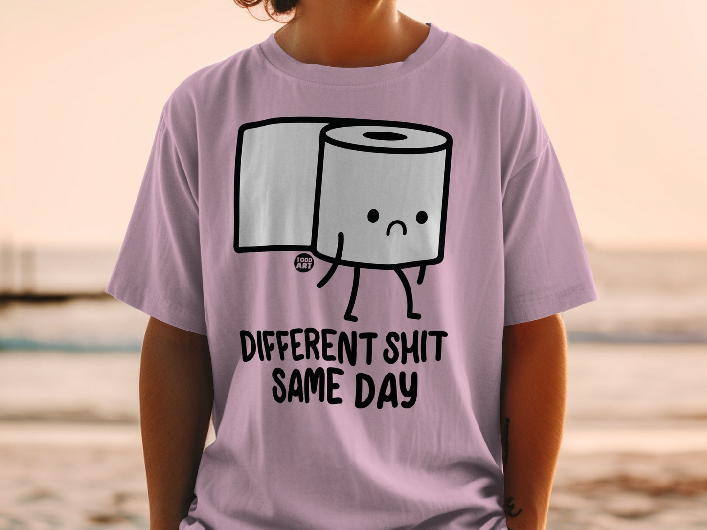 Pink t-shirt with a sad toilet paper roll character and text "DIFFERENT SHIT SAME DAY".