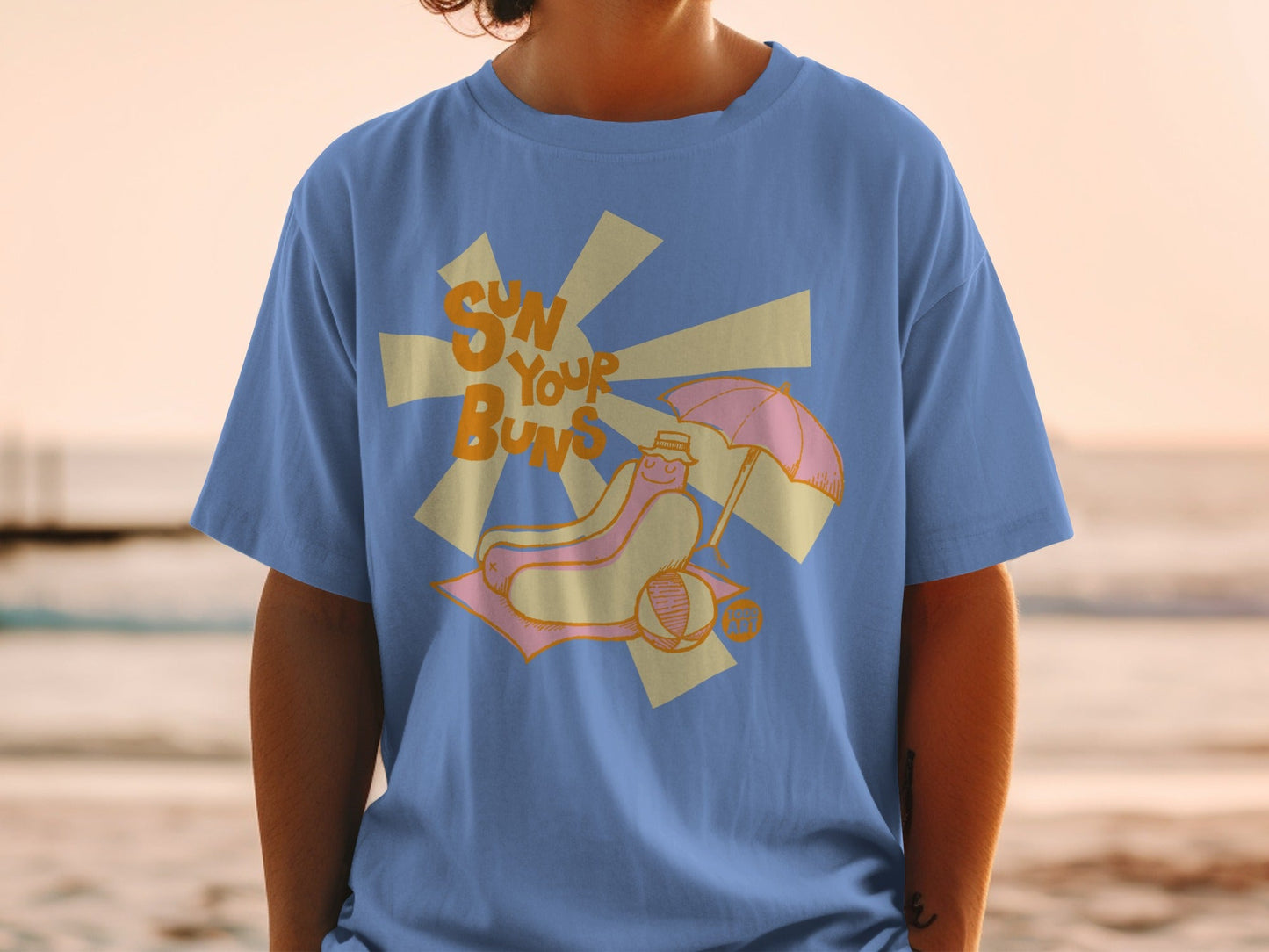 Blue t-shirt with graphic of hot dog on beach chair under umbrella.