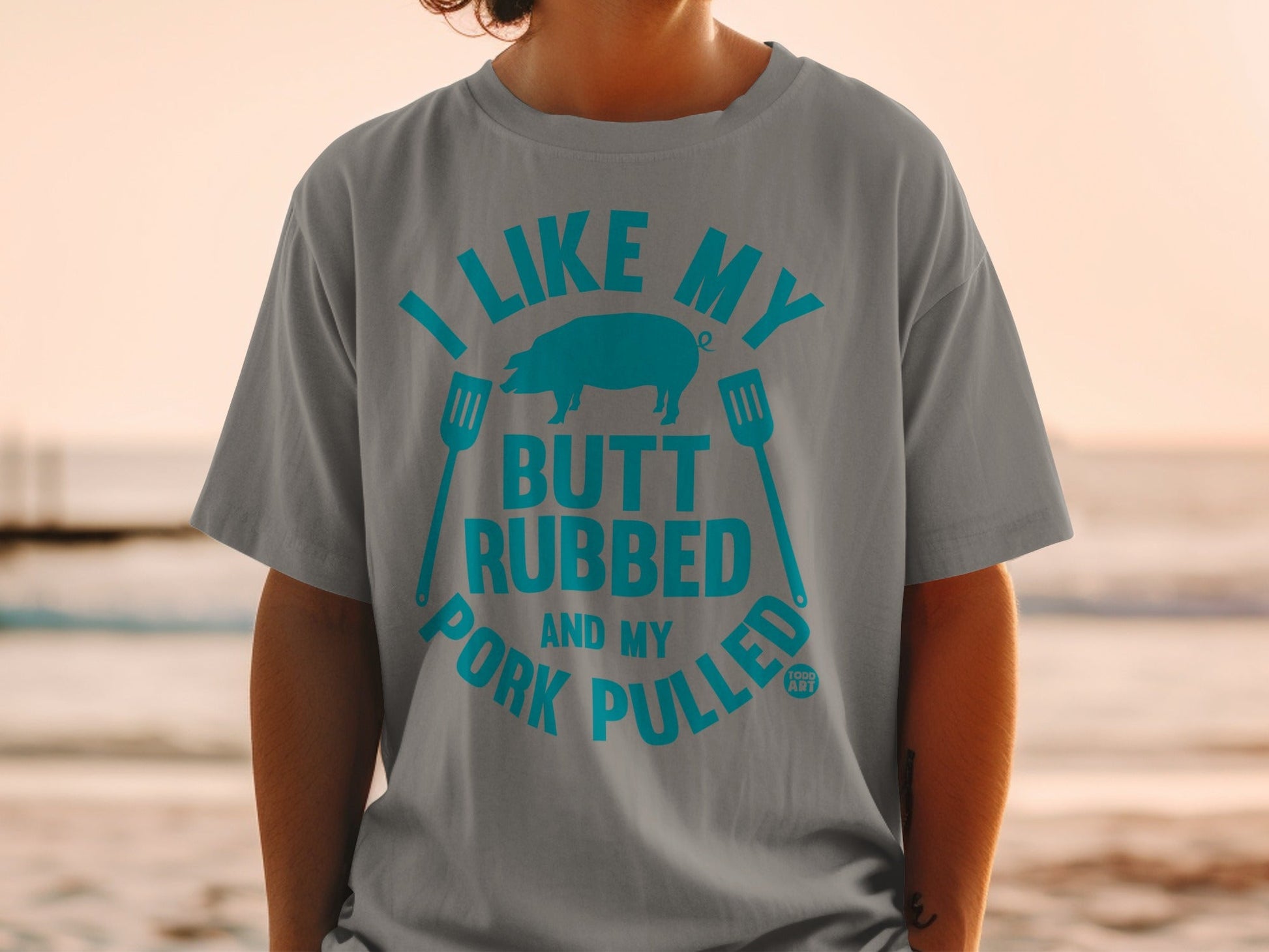 Grey t-shirt with blue text "I LIKE MY BUTT RUBBED AND MY PORK PULLED" and a pig silhouette.