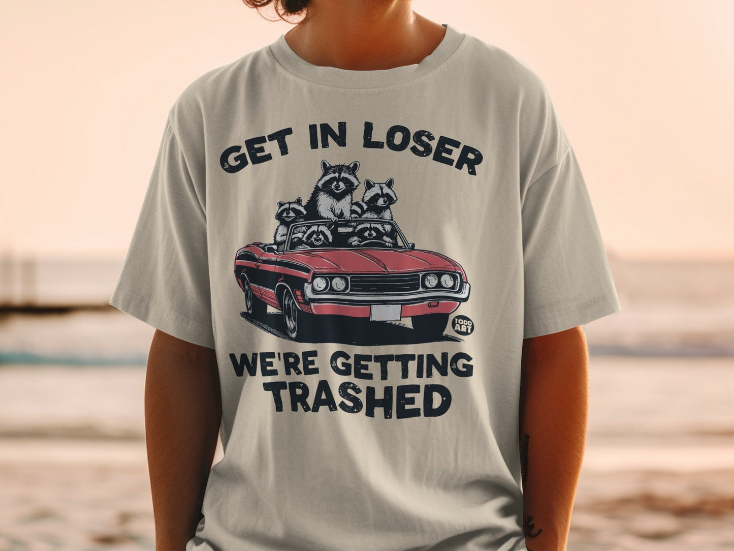 T-shirt with raccoons in a convertible, text "GET IN LOSER WE'RE GETTING TRASHED".