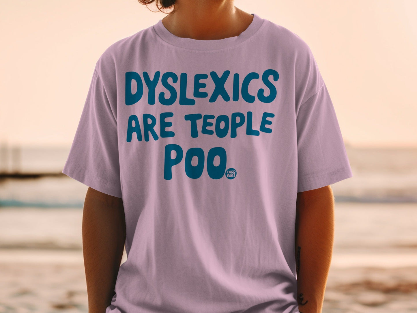 Lavender t-shirt with blue text reading "DYSLEXICS ARE TEOOPLE POO".