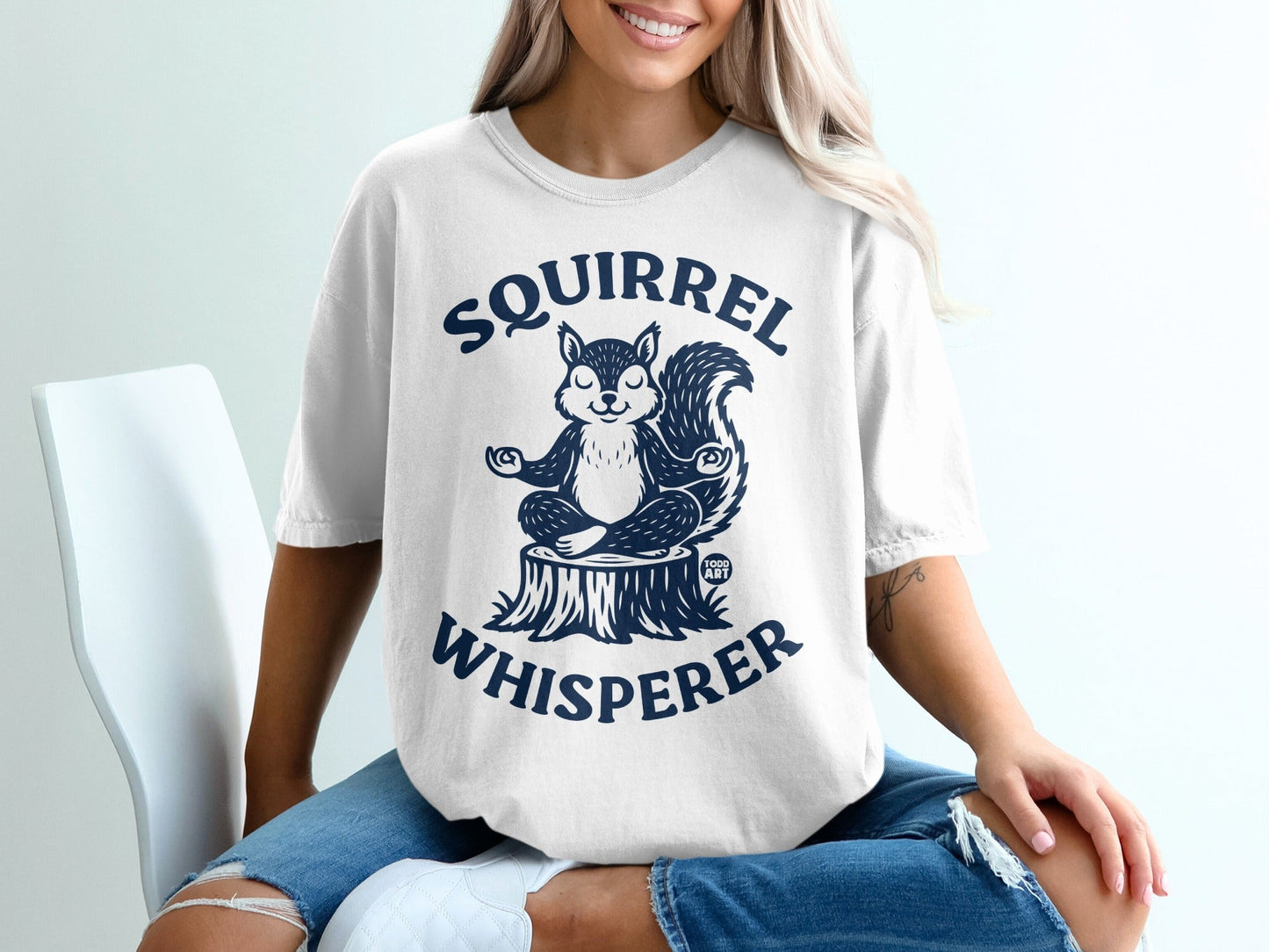 White t-shirt with a meditating squirrel graphic and "SQUIRREL WHISPERER" text.